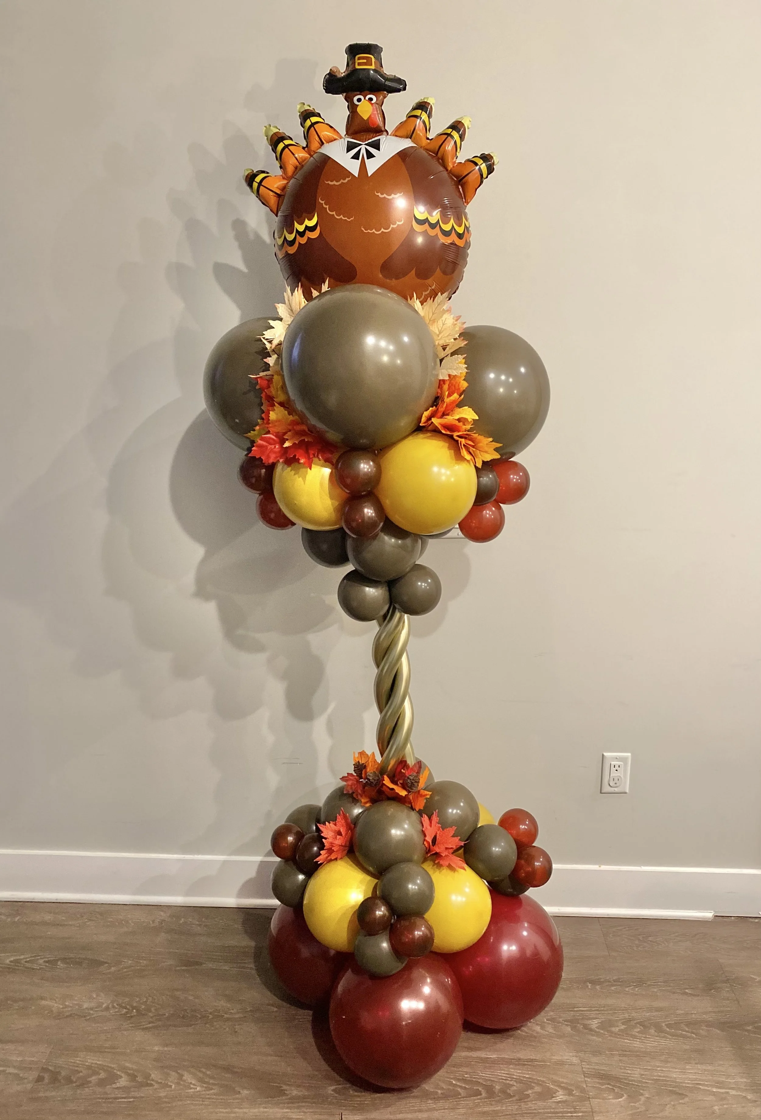 Balloon column with autumn leaves and a turkey balloon wearing a pilgrim hat at the top, celebrating Thanksgiving.