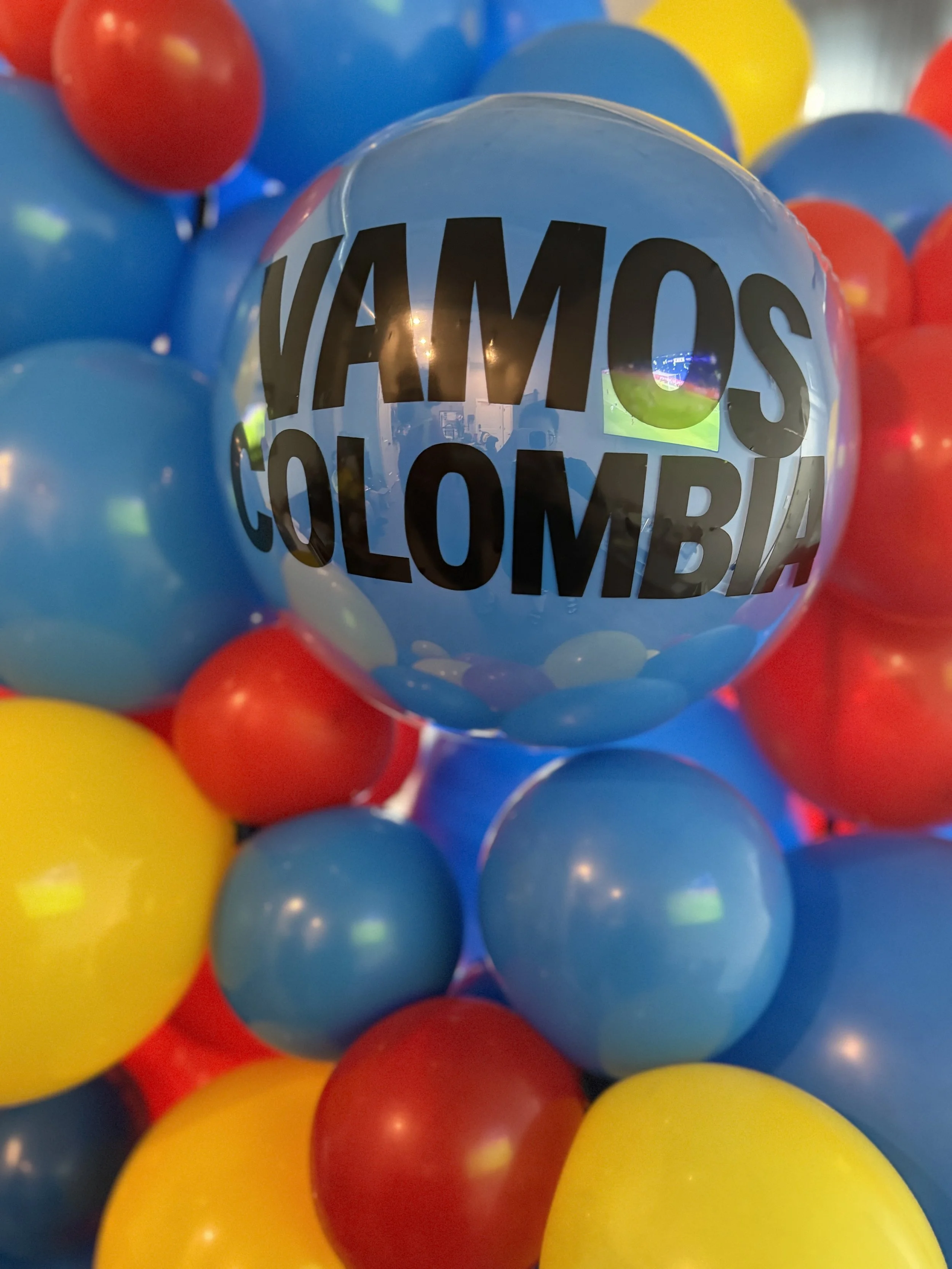 Blue balloon with black text that reads 'VAMOS COLOMBIA' surrounded by red, yellow, and blue balloons.