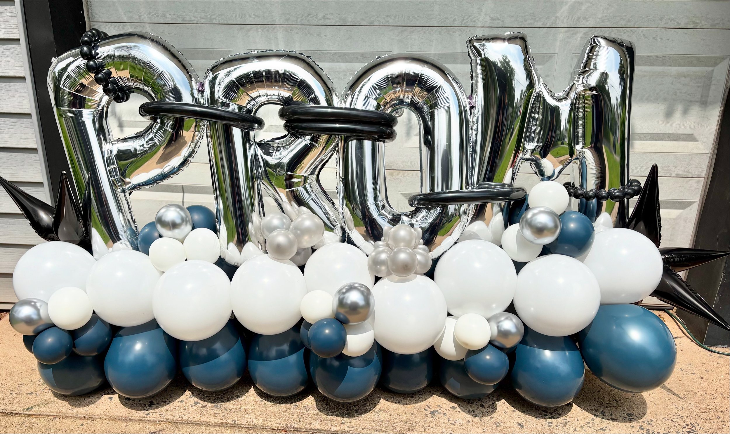Balloon display spelling out 'PROM' with black, white, silver, and dark blue balloons, some shaped as stars.