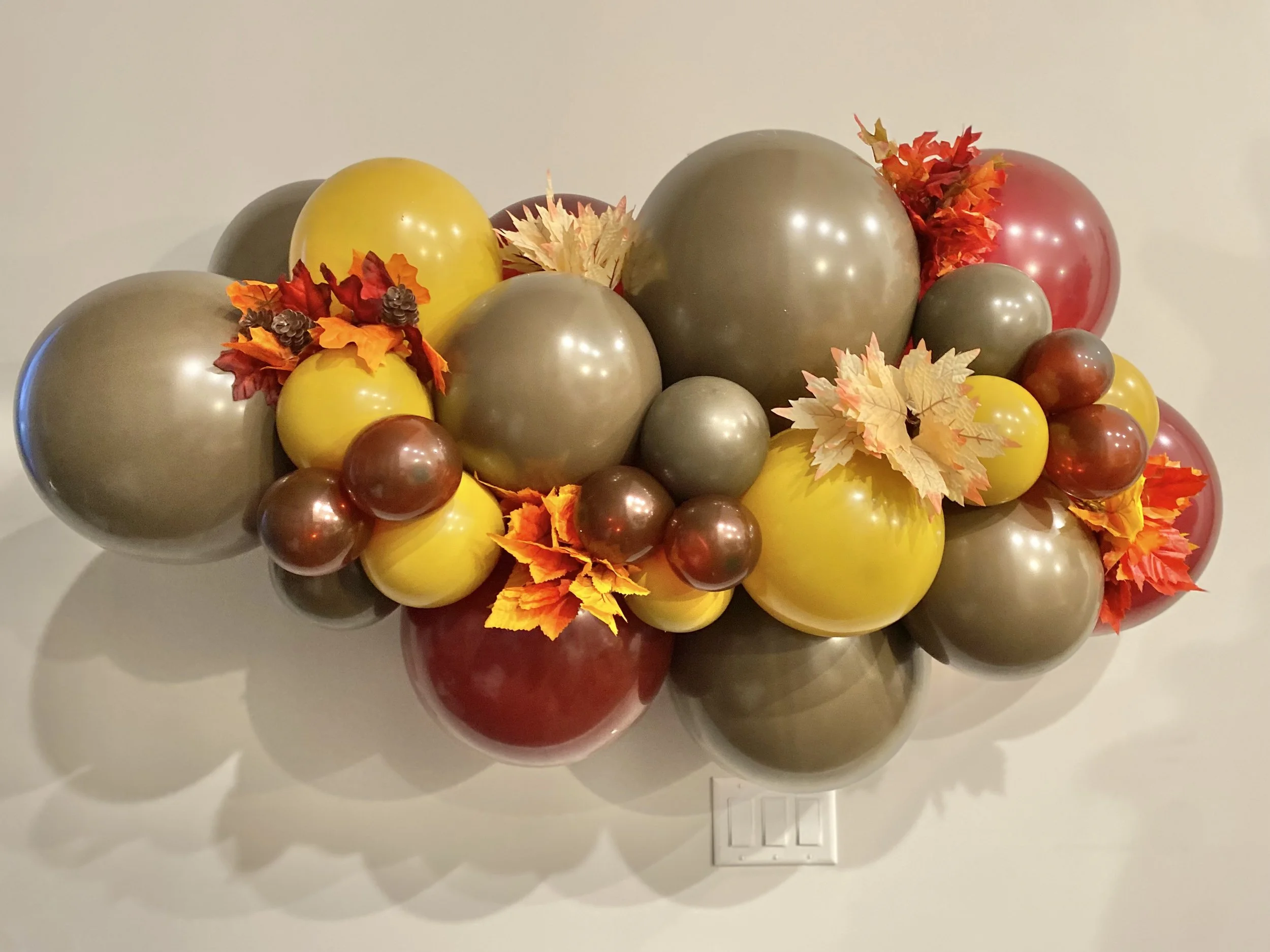 Decorative arrangement of assorted balloons in fall colors with artificial autumn leaves.