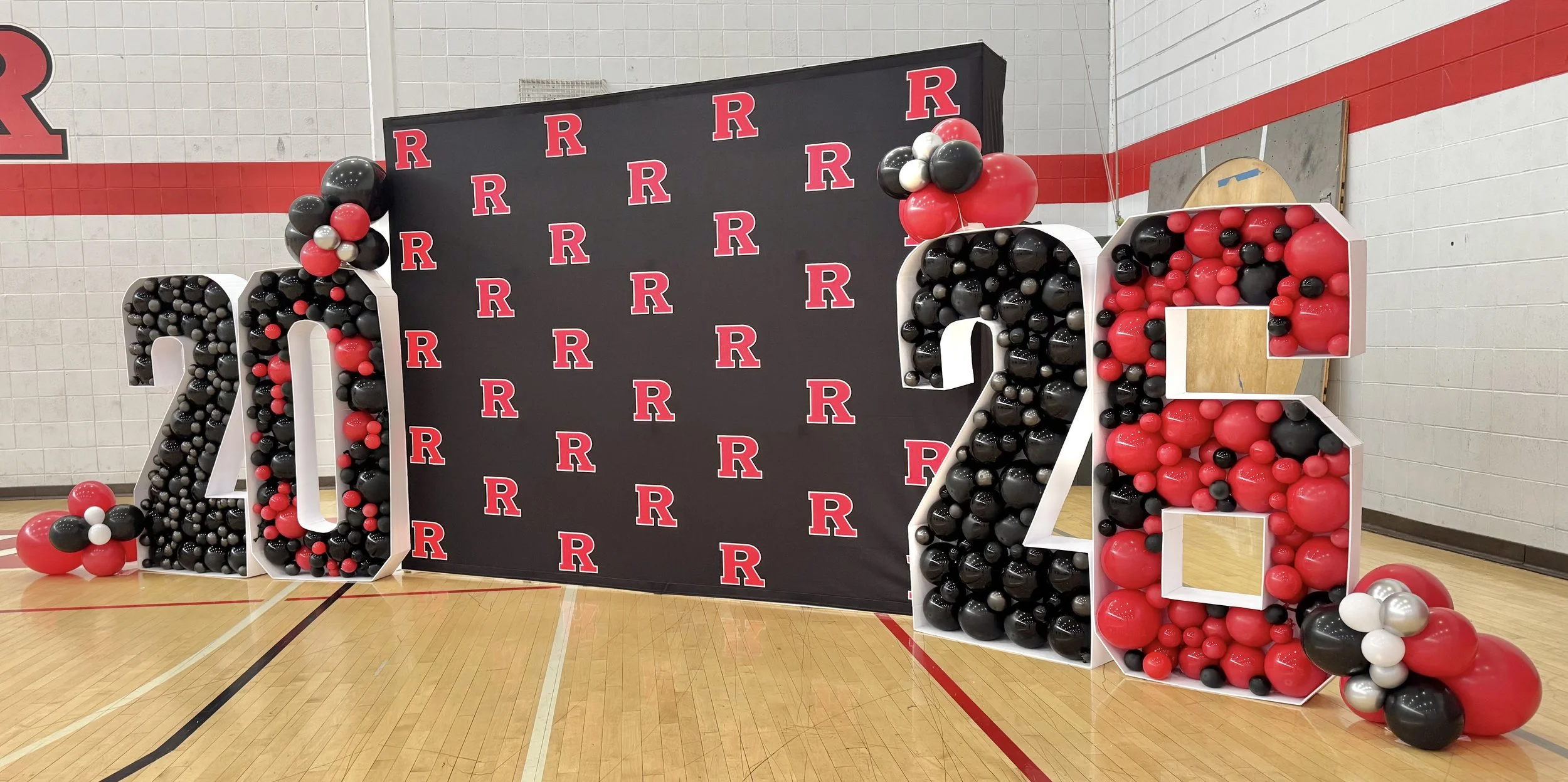 Large decorative display featuring the numbers 2023 made of balloons in black, red, gray, and white, with a backdrop decorated with red 'R' logos, possibly for a university or school event.