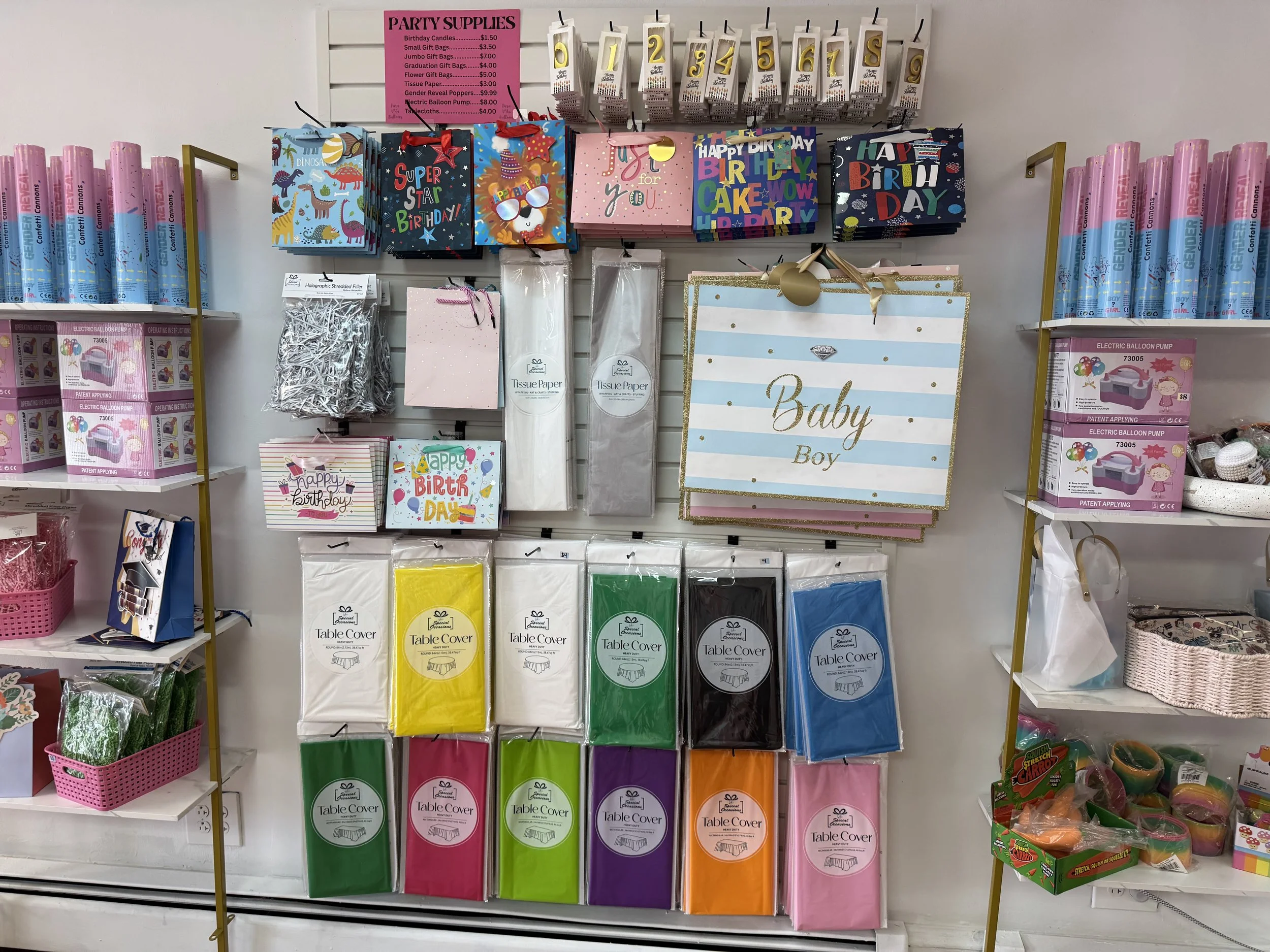 Display of colorful gift bags, table covers, balloons, and party decorations in a store section.