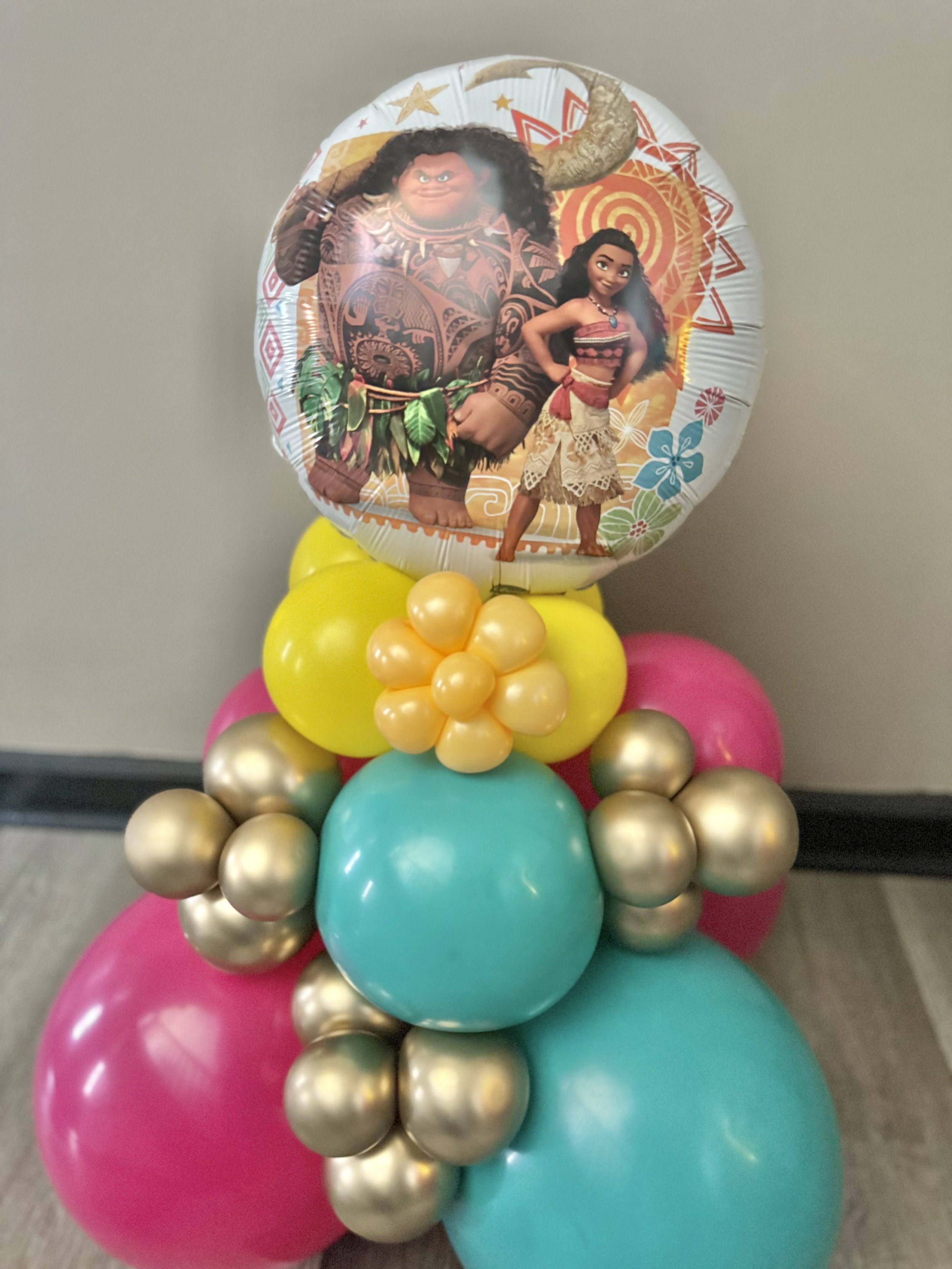 Colorful balloon bouquet featuring a large round balloon with characters from Disney's Moana, surrounded by pink, blue, yellow, and gold balloons.