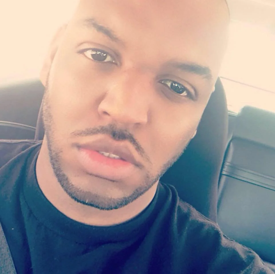 Close-up of a person sitting in a car, wearing a black shirt, with a seatbelt visible.