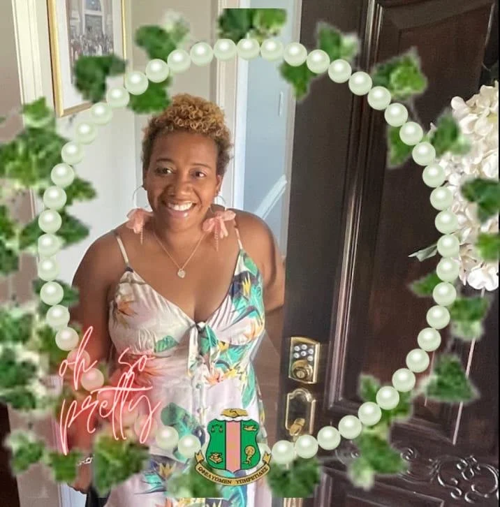 Smiling woman in floral dress with pearl and ivy frame, floral earrings, and a sorority crest.