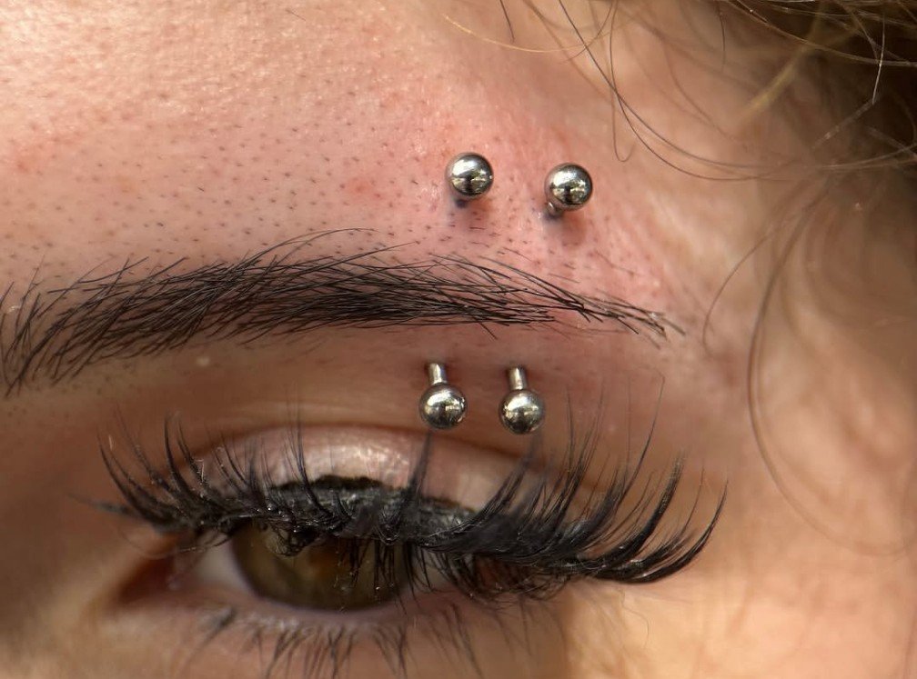 Closeup of a double eyebrow piercing on a woman using 16g implant grade titanium curved barbells. An image of a girl with a set of eyebrow piercings performed at a professional body piercing studio. a picture of a woman with long eyelashes and a doub