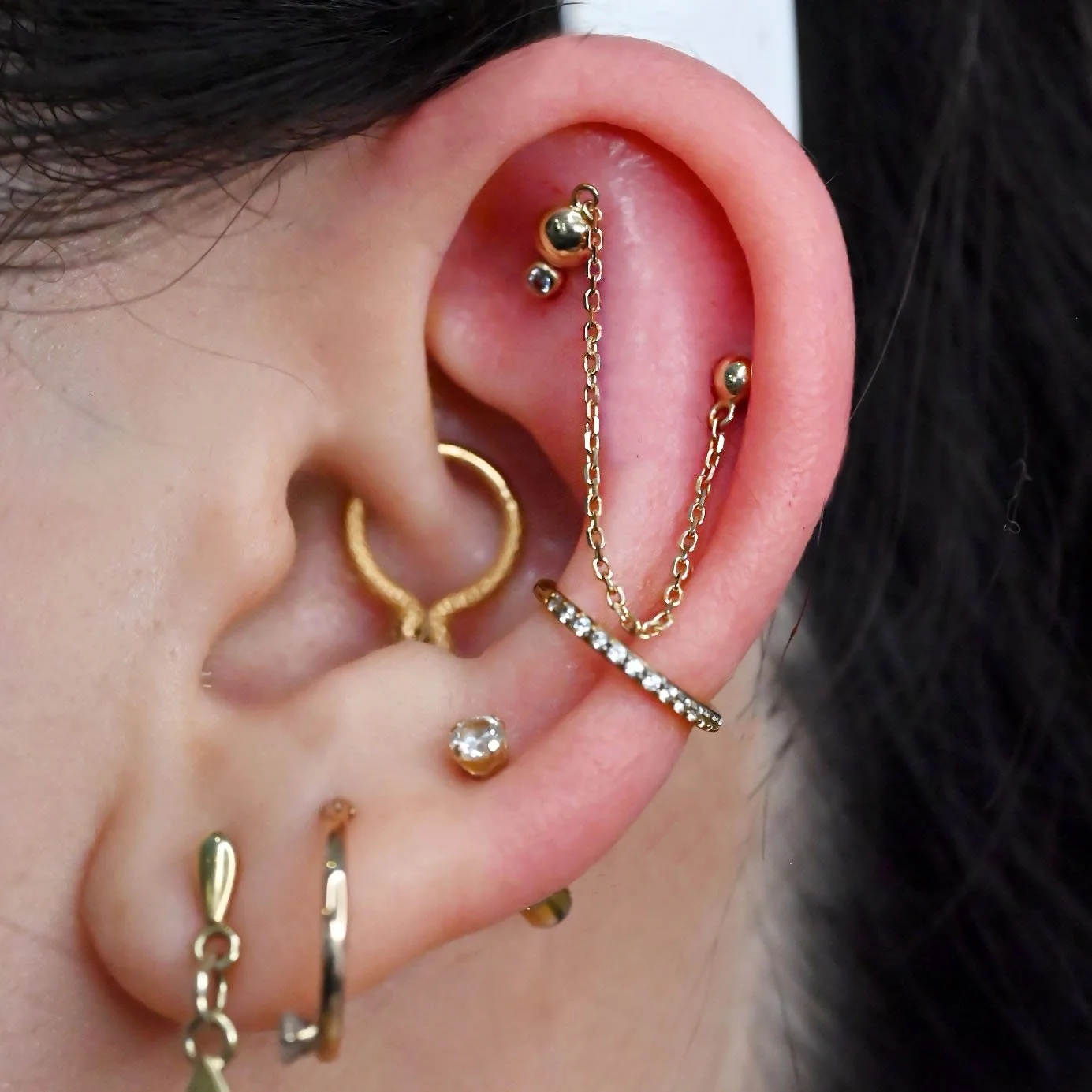 flat and helix piercings pierced with a yellow gold chain and stud. double helix piercings pierced by dee at coven body arts with 14k solid yellow gold body jewelry from junipurr body jewelry. two ear piercings connected with a yellow gold chain pier