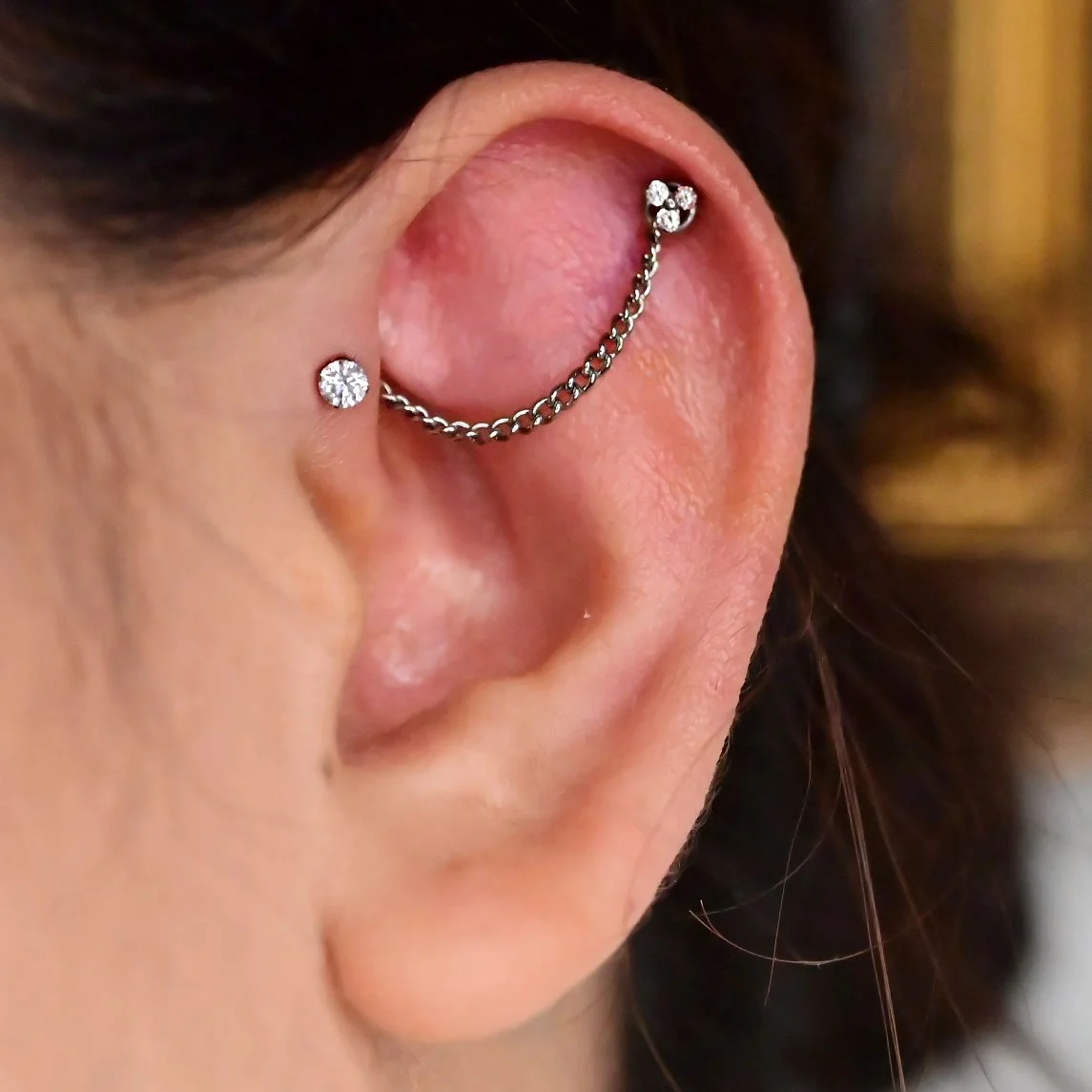 a helix piercing and a forward helix piercing done in a professional body piercing studio in calgary, alberta. two piercings connected with a chain to make an industrial piercing. woman with two ear piercings connected with a titanium chain. ear pier