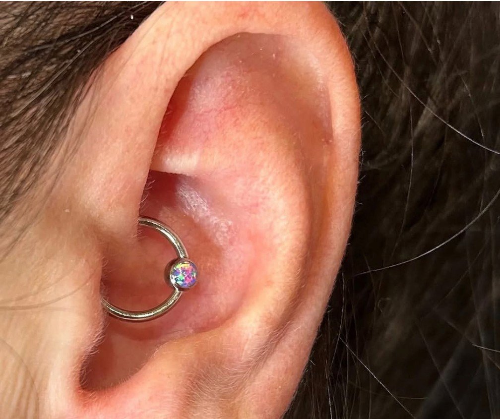 fresh daith piercing performed with an implant grade titanium captive bead ring by a professional body piercer at a professional body piercing studio. closeup image of a daith piercing in a womans ear with a silver hoop. a ring in a daith piercing, h