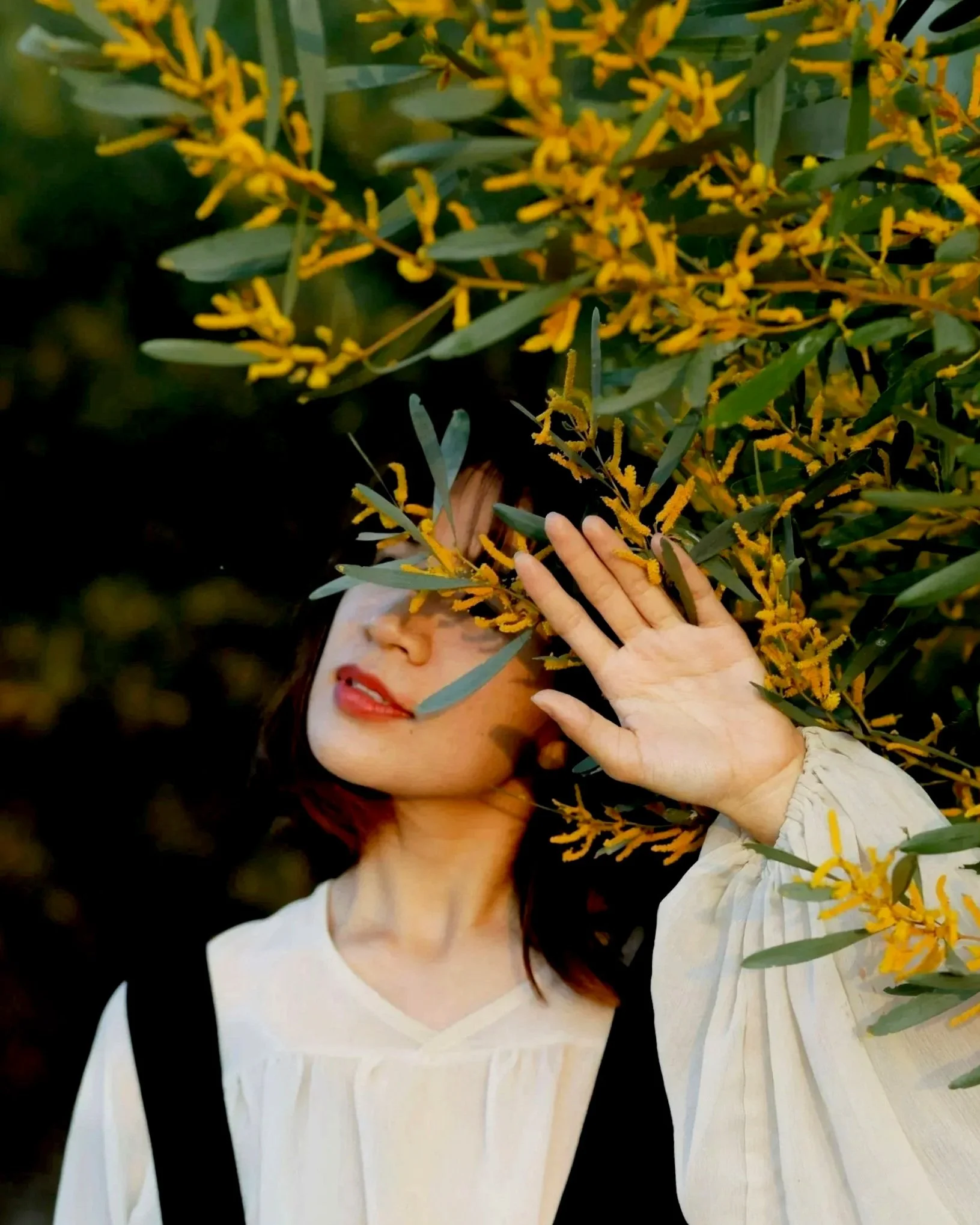 Girl behind green and yellow tree with her left arm raised
