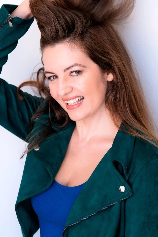 Actress Lorena Fernández in a yellow top, looking directly at the camera against a light textured wall.