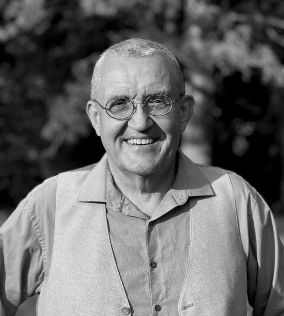 image: Male therapist with short white hair and round glasses standing outside smiling at the camera