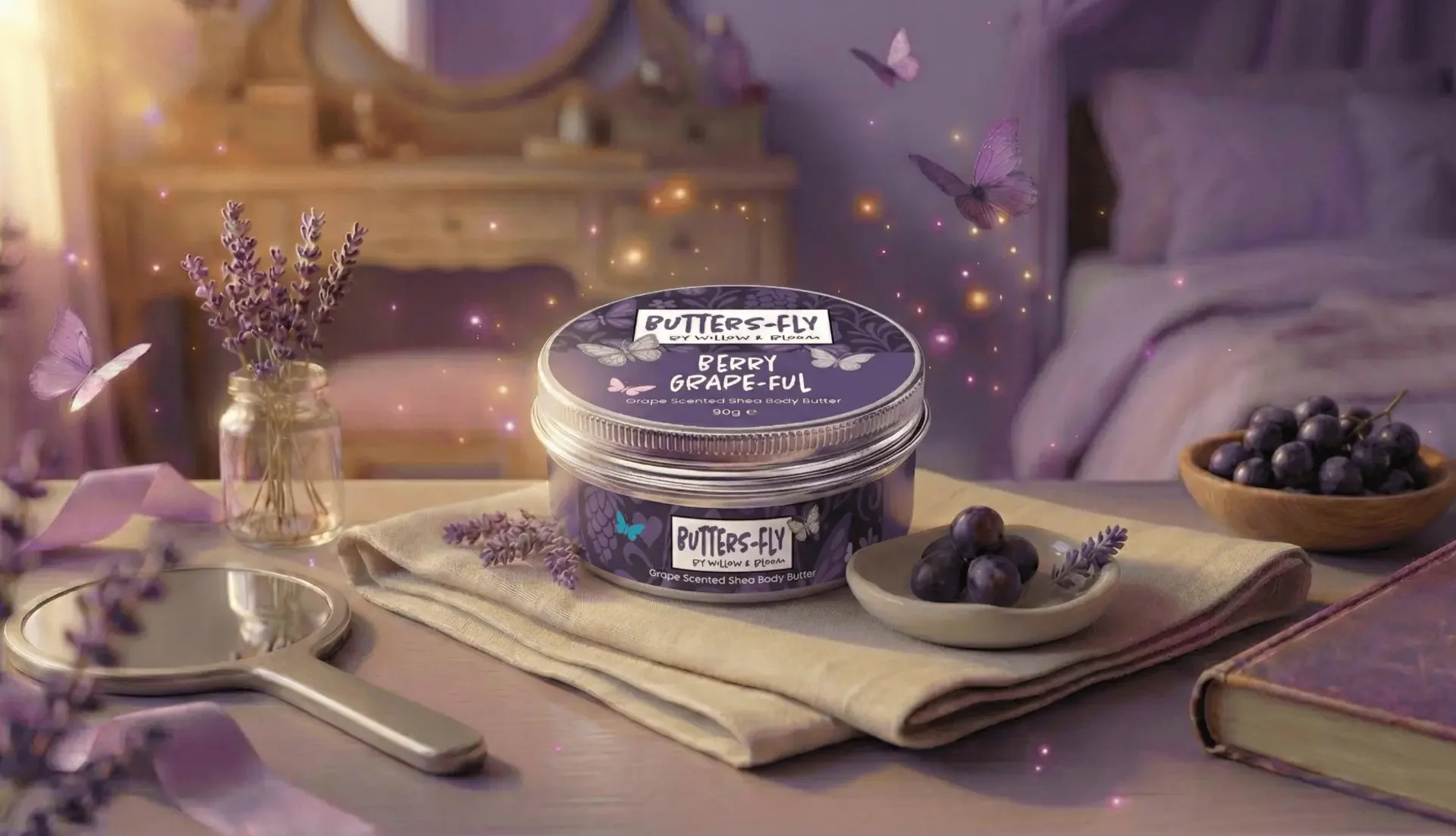 A jar of buttery body butter labeled 'Berry Grape-full' with purple grapes, lavender flowers, and butterflies around it, placed on a table with a mirror and a book.