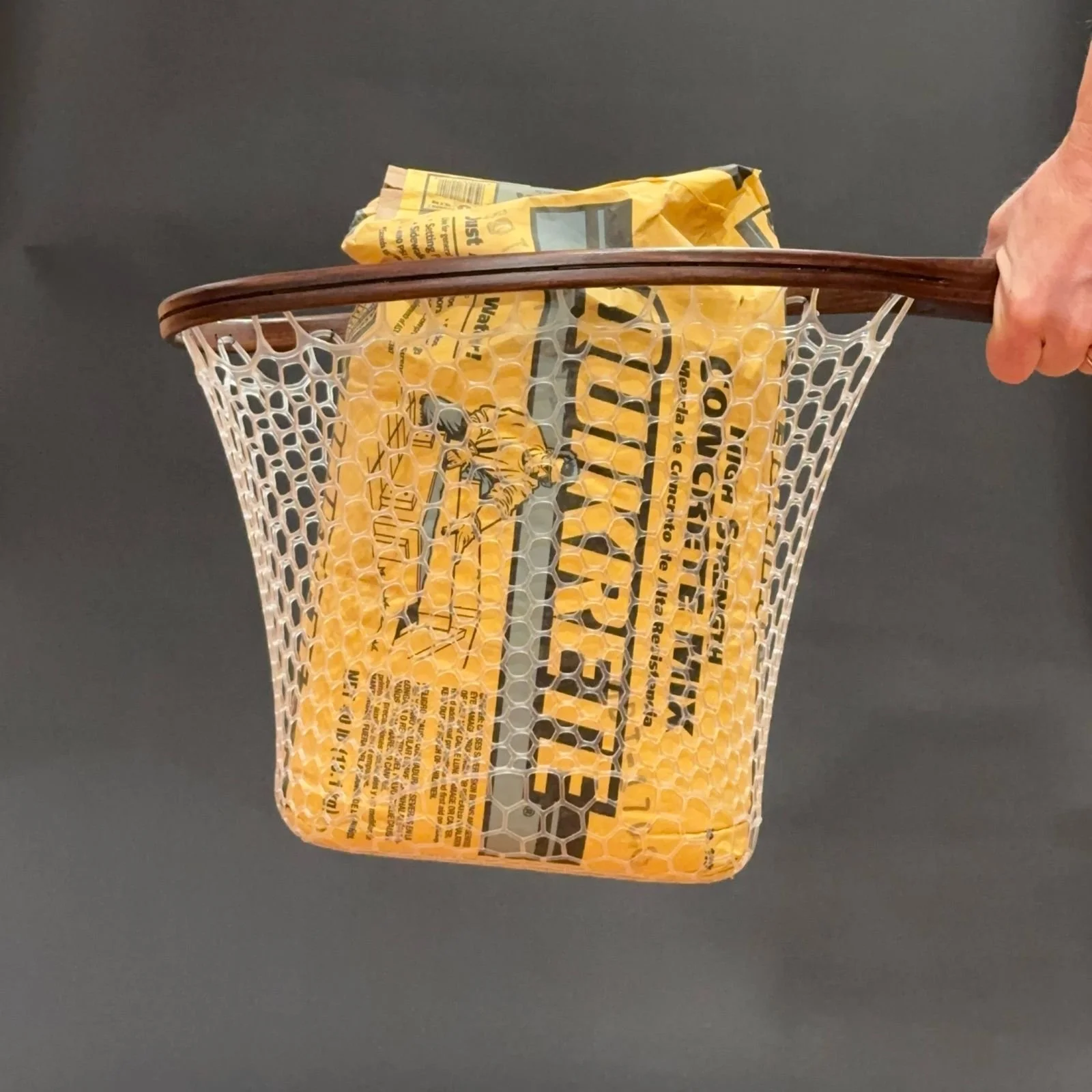 A RockSpring Rafffy Mid Run wooden landing net holding a 40 lb bag of concrete mix in its netting, demonstrating the exceptional strength and durability of RockSpring Nets