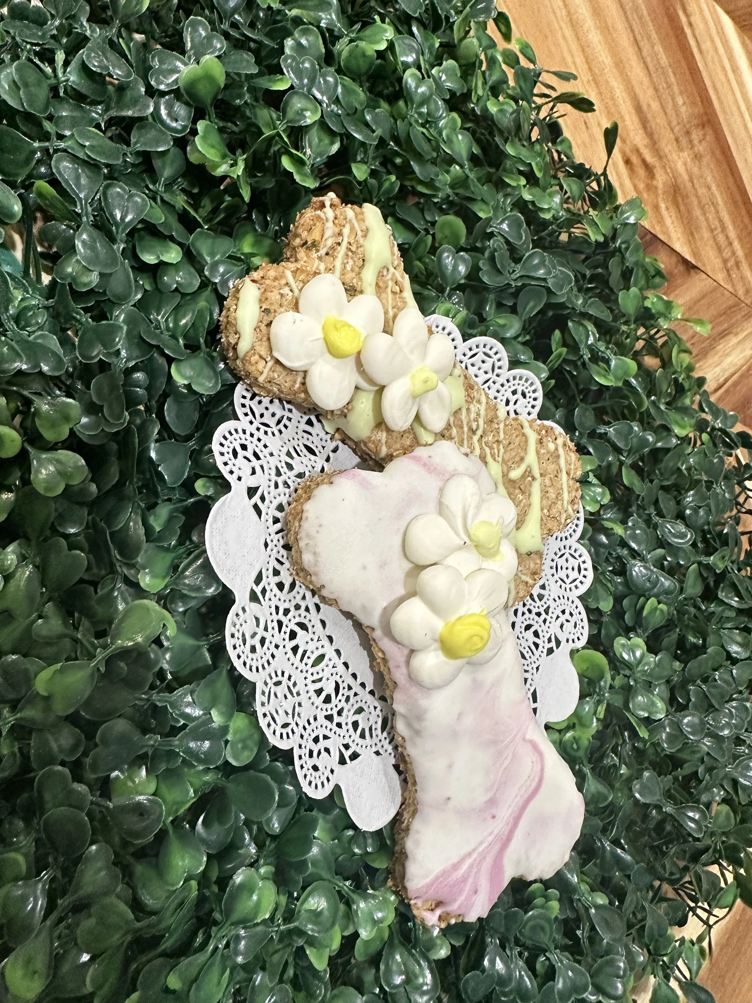 Dog bone-shaped cookies with icing and decorative flowers on a leafy background.