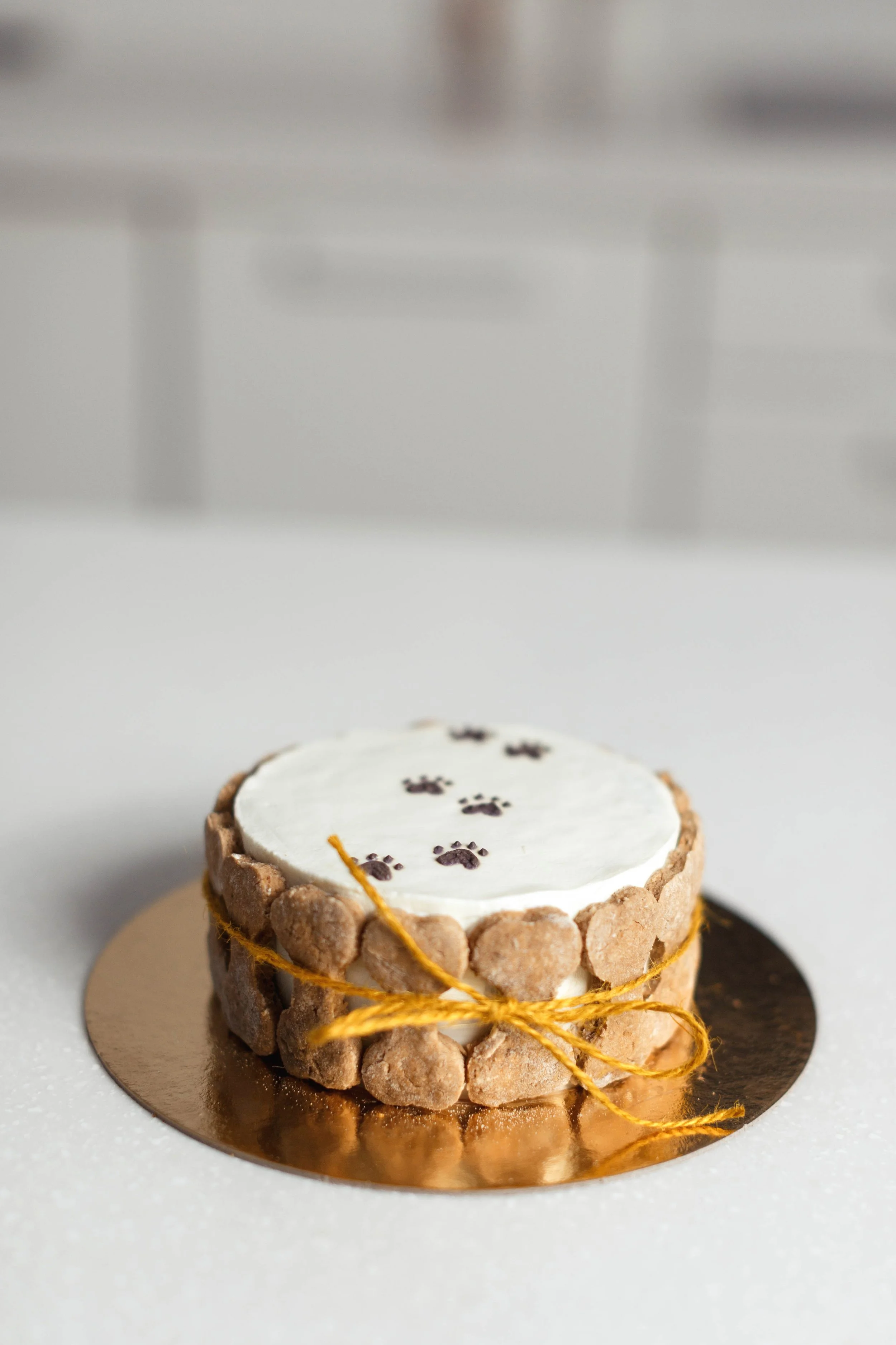 Small cake decorated with paw prints on top, surrounded by cookies, tied with a yellow string, on a round platter.