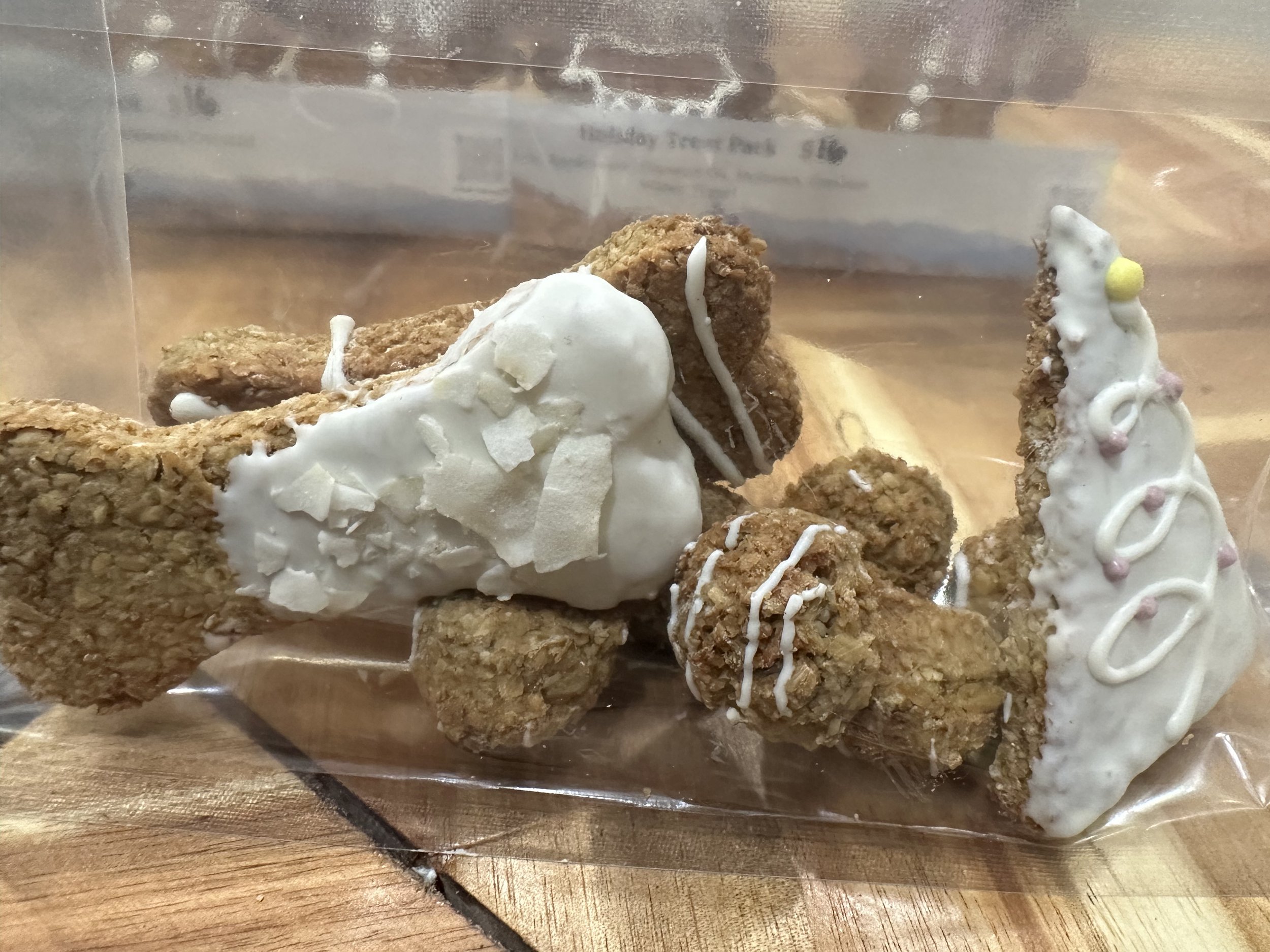 A variety of dog treats in a plastic bag, including bone-shaped and triangular treats, coated with white icing and pink decorations.