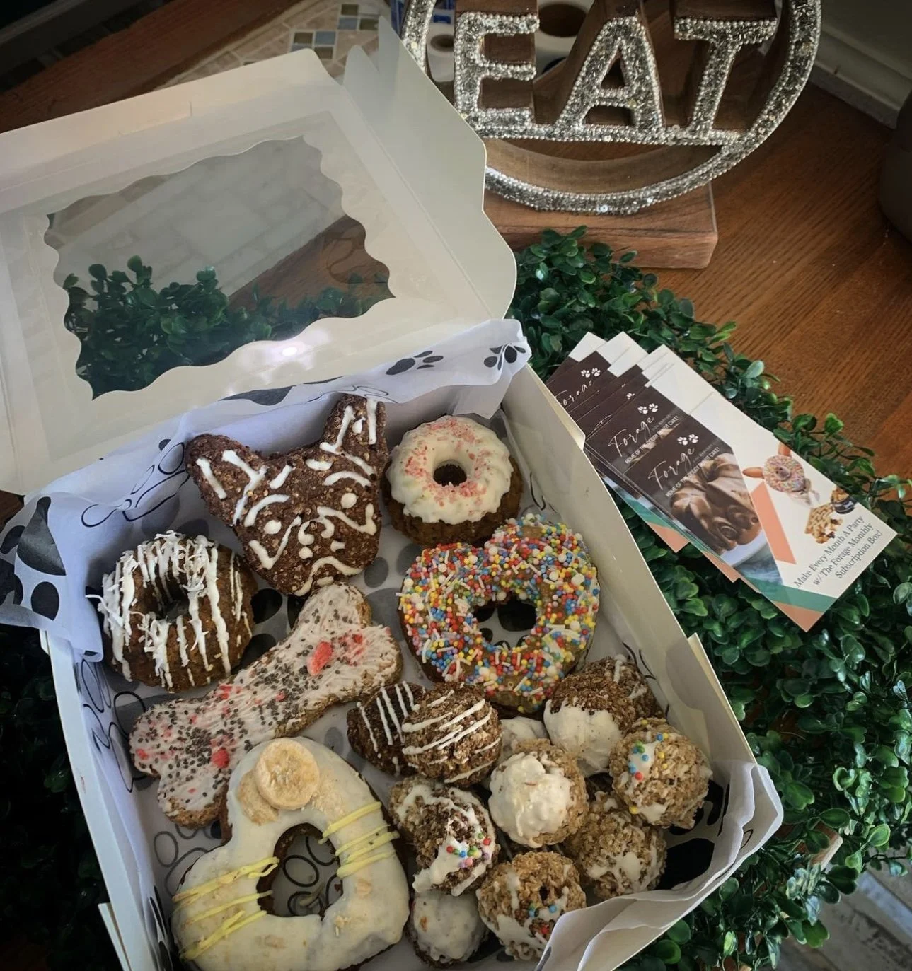 Box of decorative dog treats in various shapes and toppings, placed on a table with brochures nearby.