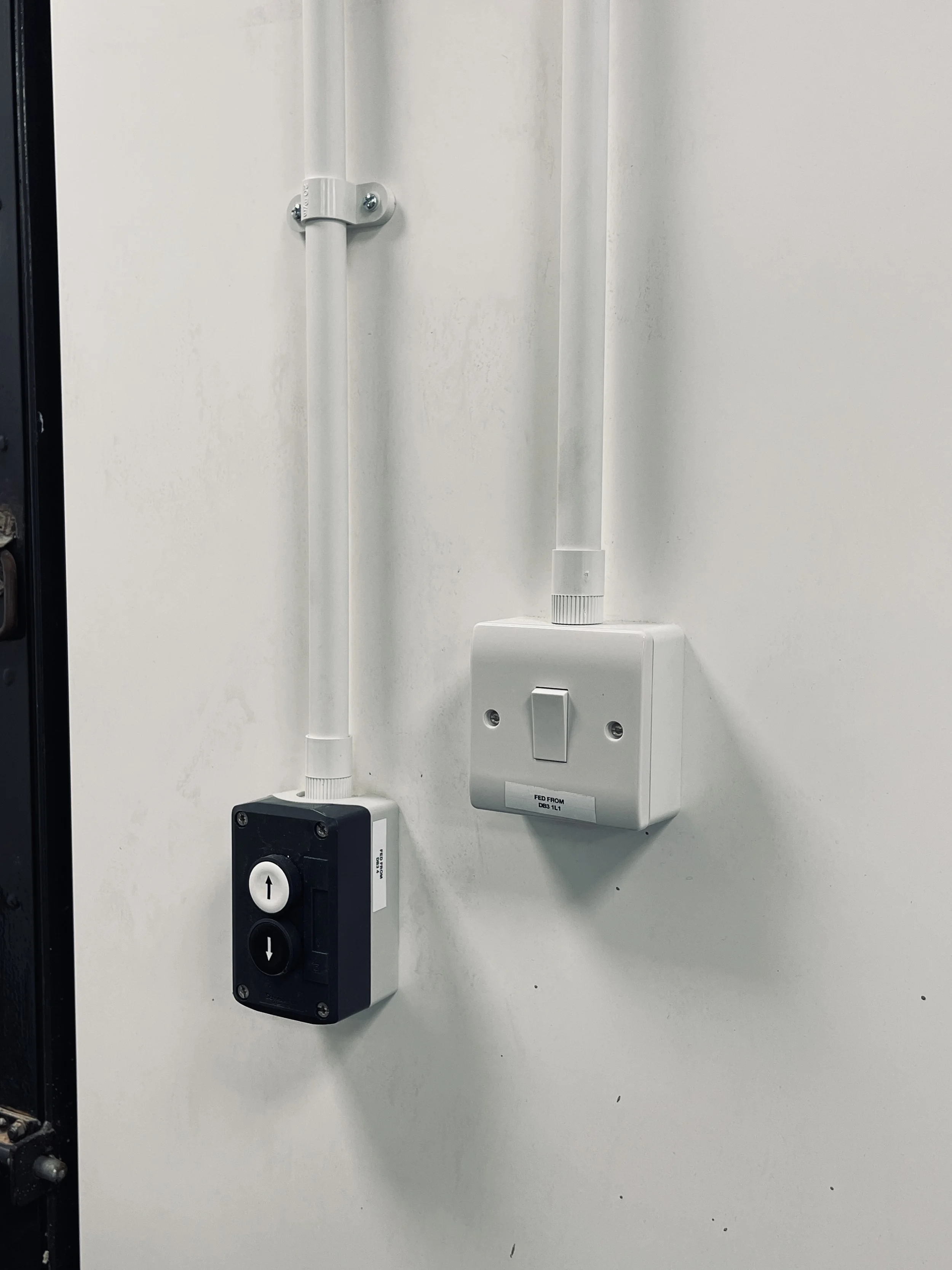 Electrical switch and control box mounted on a white wall with electrical conduit pipe.