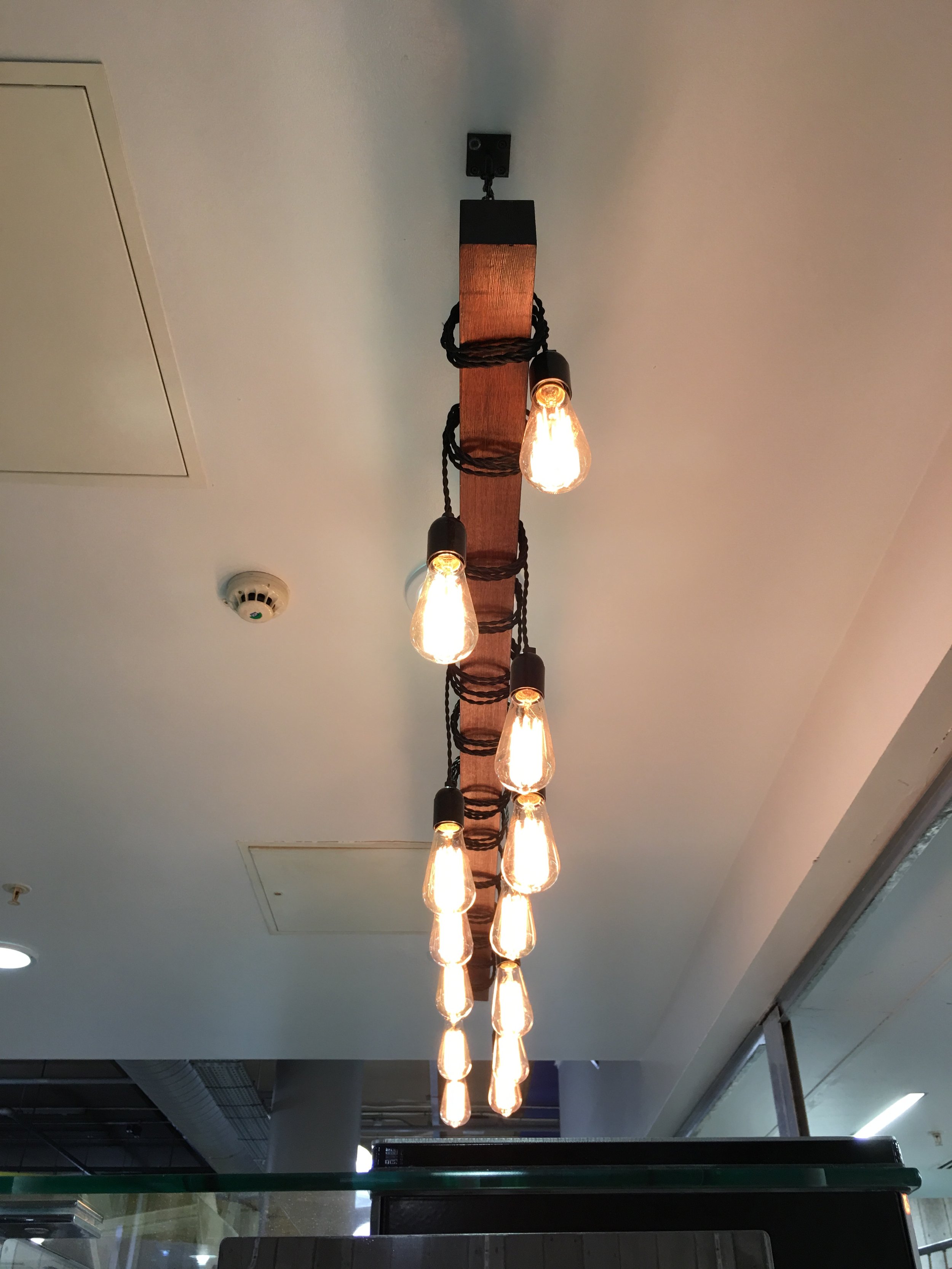 Industrial-style chandelier with multiple Edison bulbs hanging from a wooden and metal fixture.