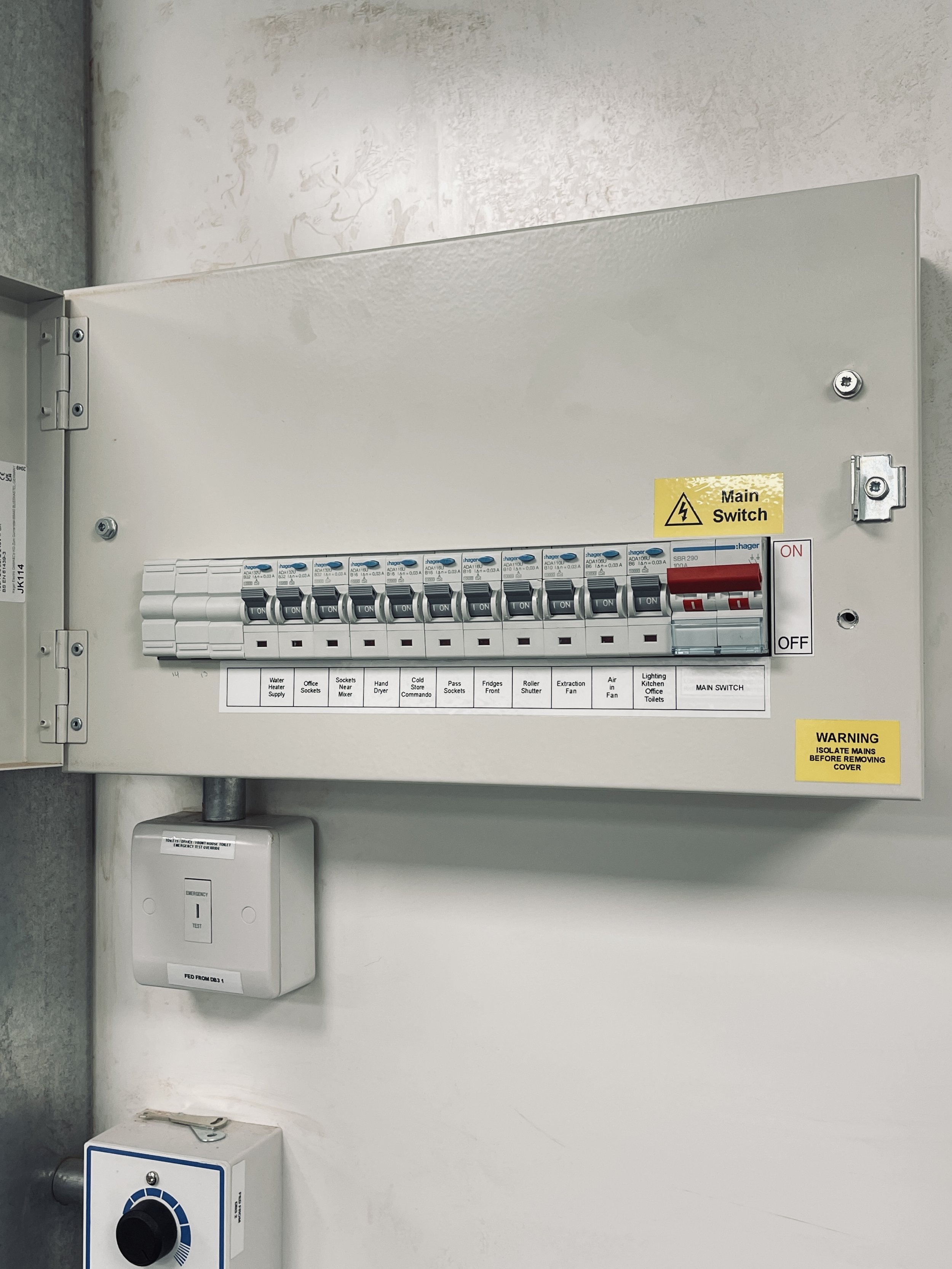 Electrical panel with circuit breakers labeled for various appliances and a main switch, mounted on a wall.