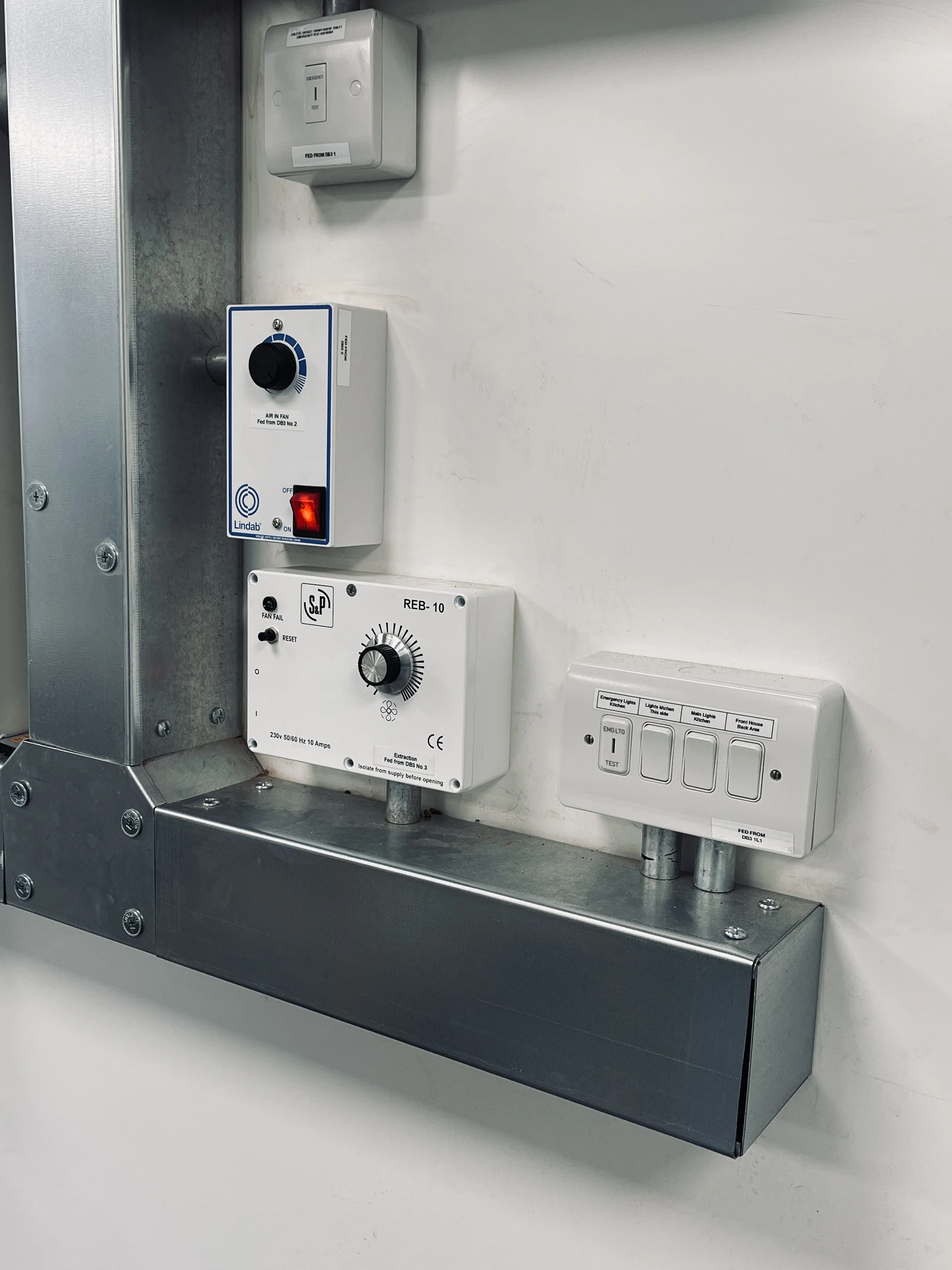 Electrical control panels and switches mounted on a white wall in an industrial or commercial setting.