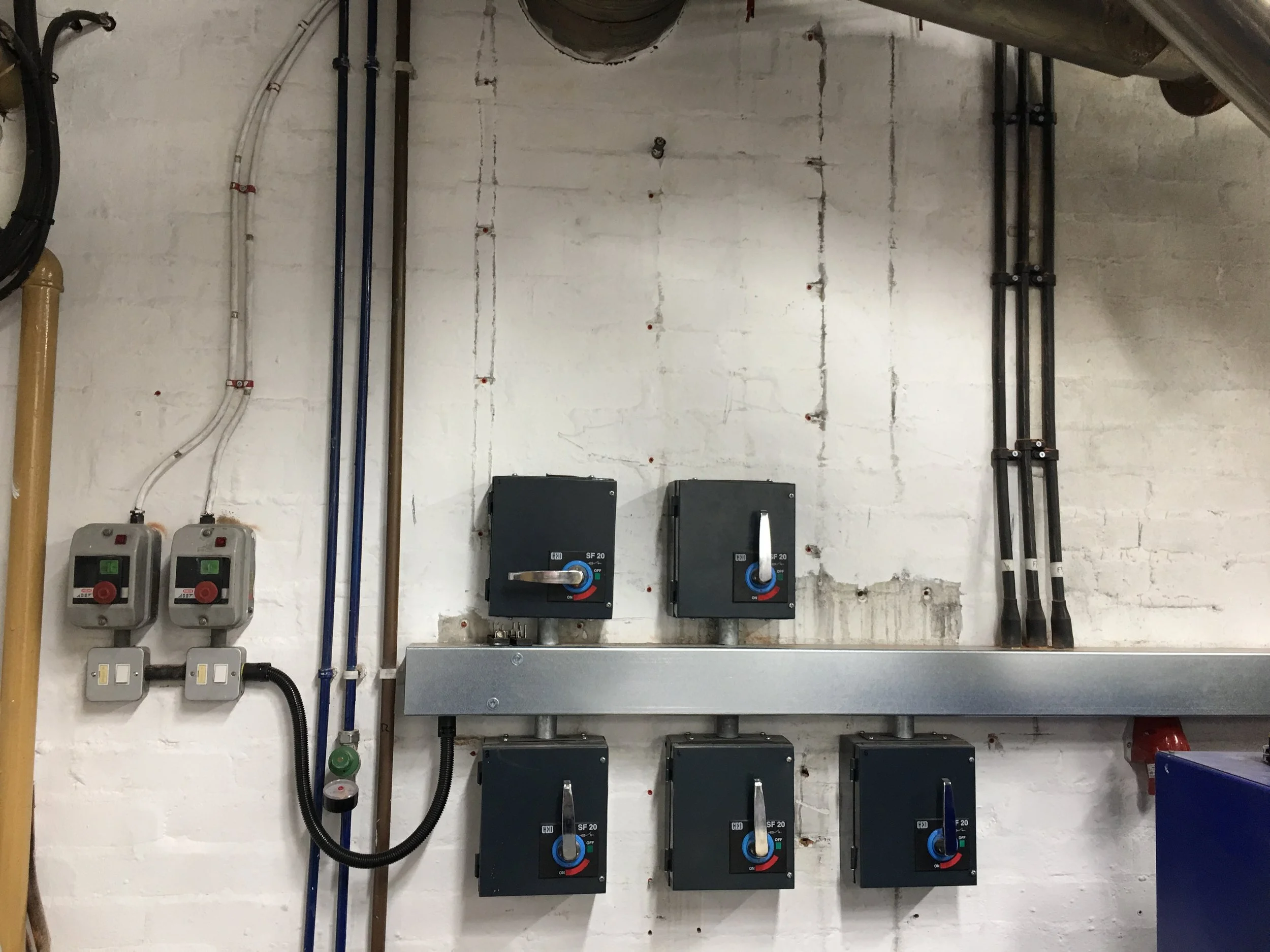 Electrical control panel and wiring on a white brick wall.
