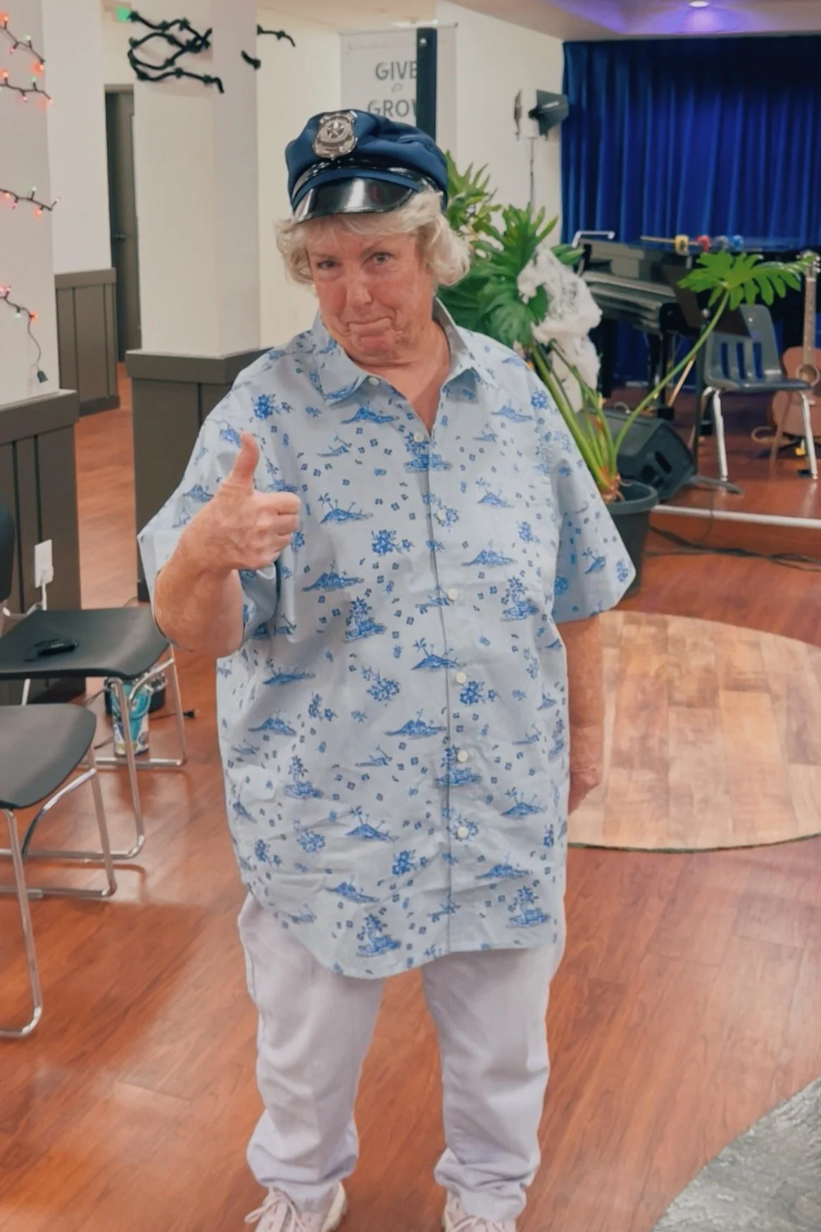 Cheryl smiles at the camera and gives a thumbs-up while wearing a police cap and costume during play rehearsal.