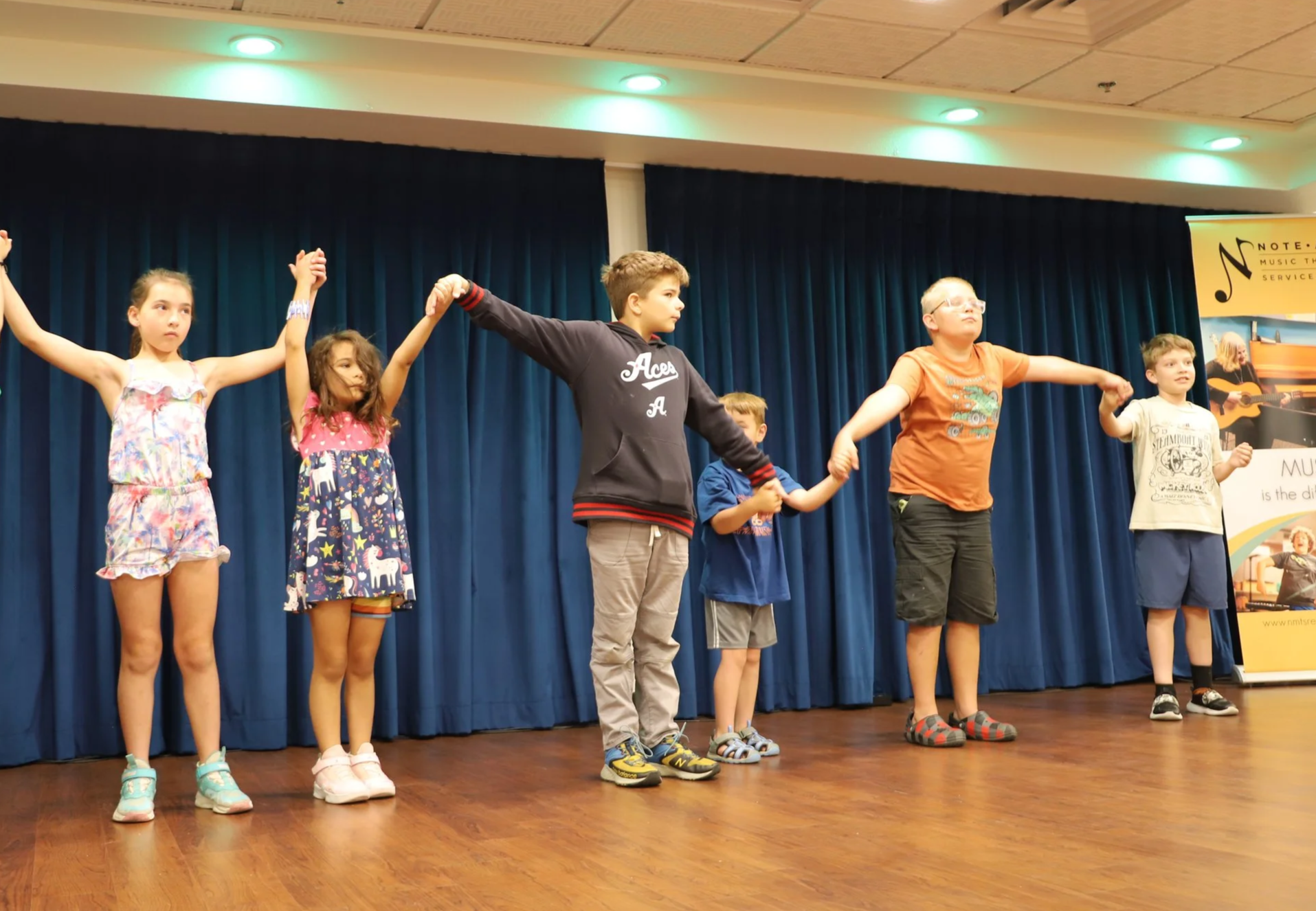 Kids on stage at NMTS preparing to take a bow after a performance at the 2025 kids summer music camp