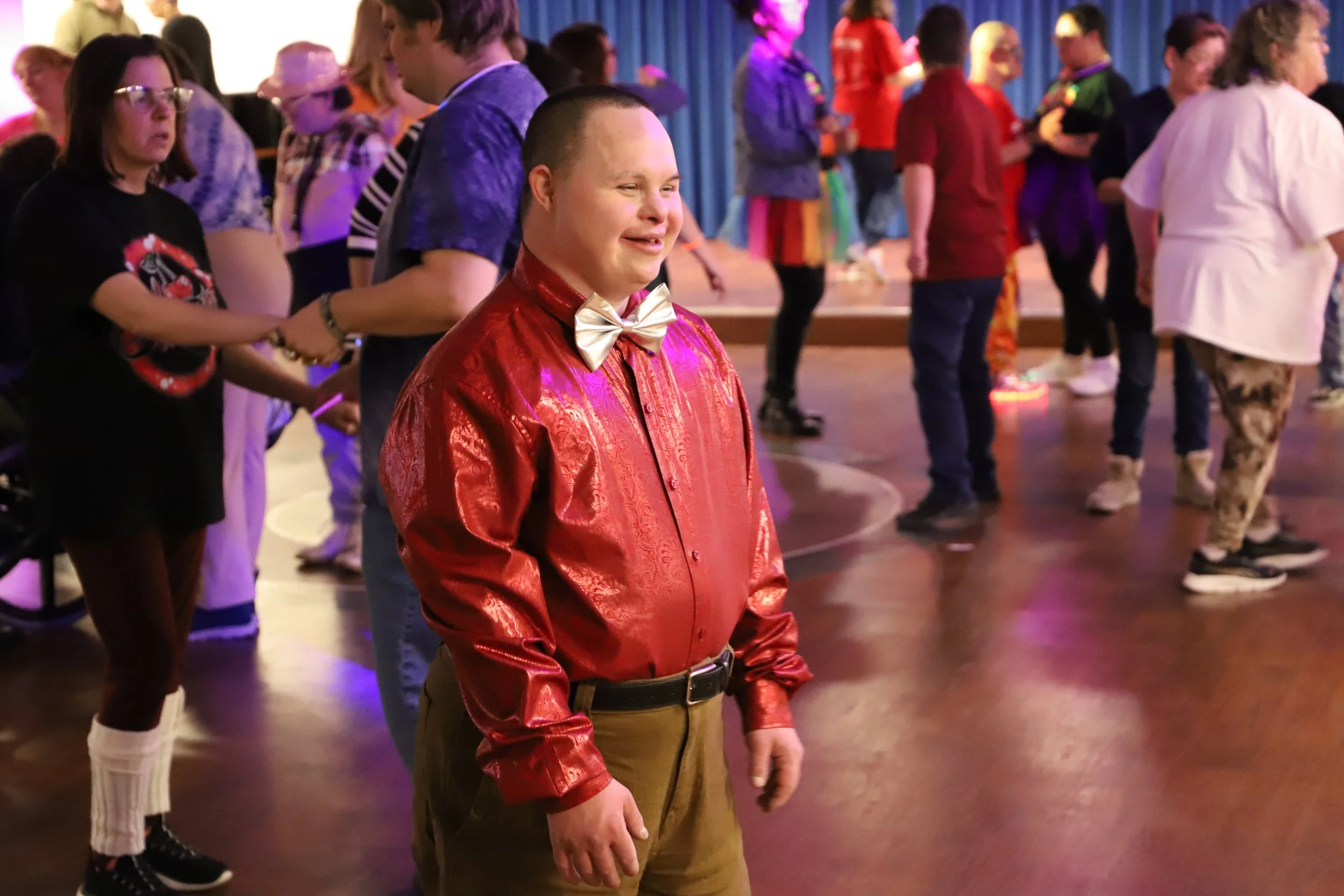 Participant smiling and dressed in a red shirt and bow tie while attending an NMTS community dance event.