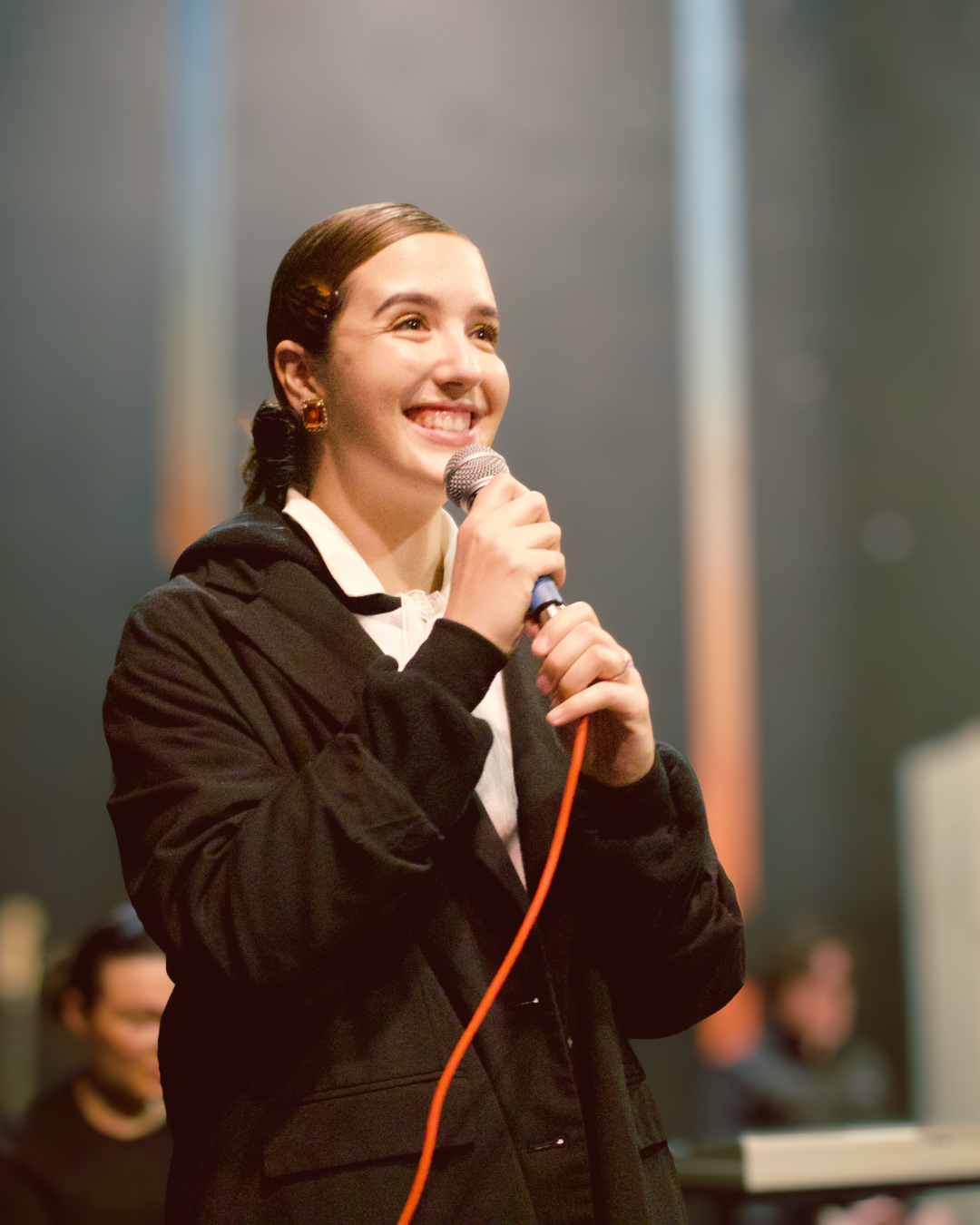 Young woman smiling and holding a microphone performing on stage.