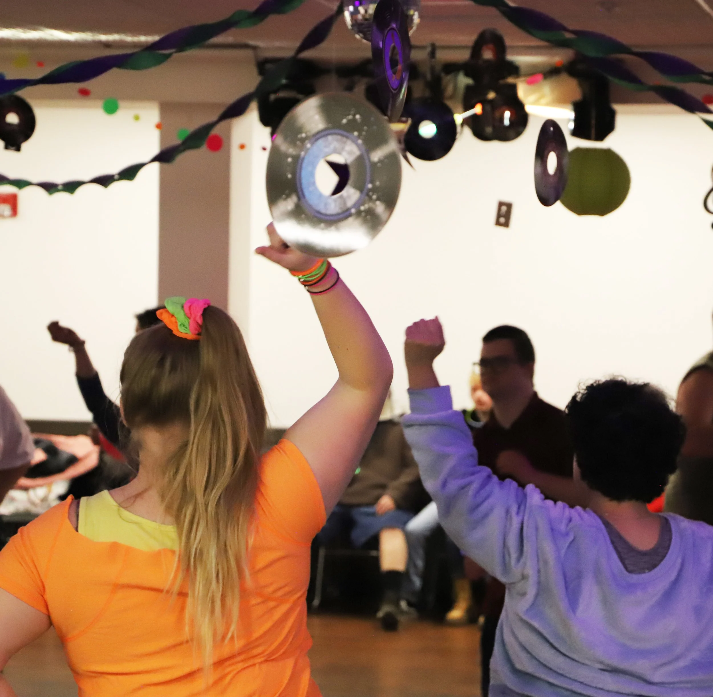 Group of people dancing with their arms raised in the air at NMTS community dance event.