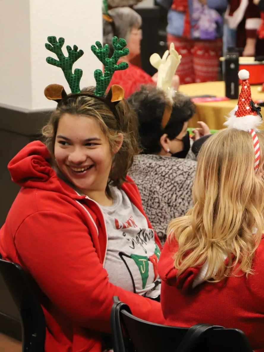 Candid of a girl in red hoodie with reindeer antlers headband smiling at last year’s NMTS holiday party.