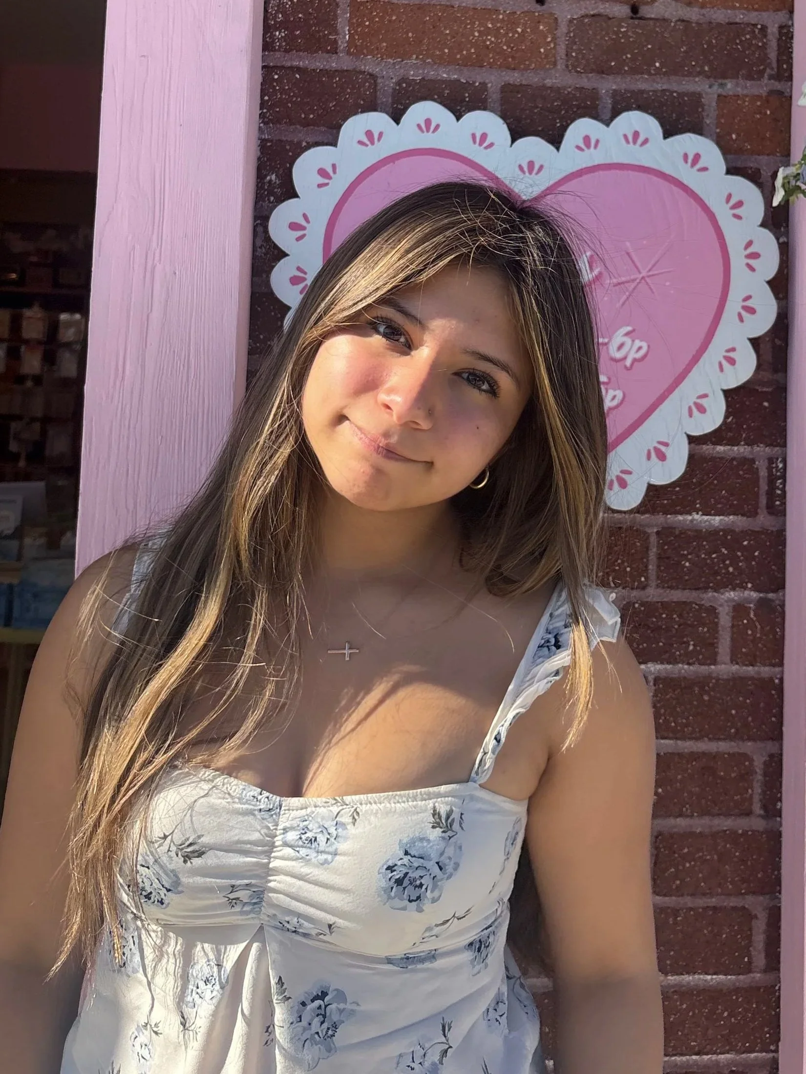 Photo of Erin wearing a flowered top and a heart on the wall behind her.