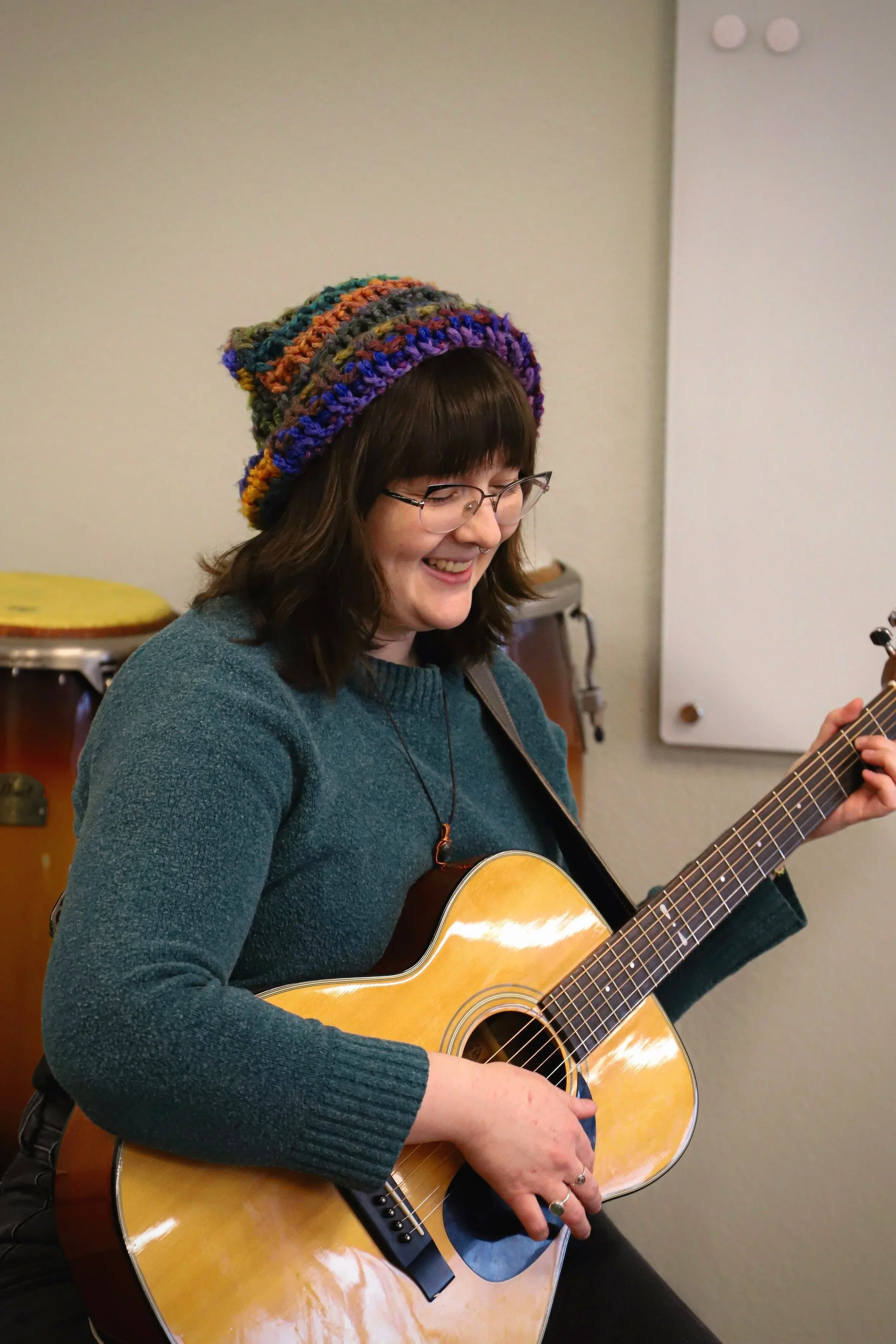 Emma, NMTS music therapy intern, smiling while playing guitar.