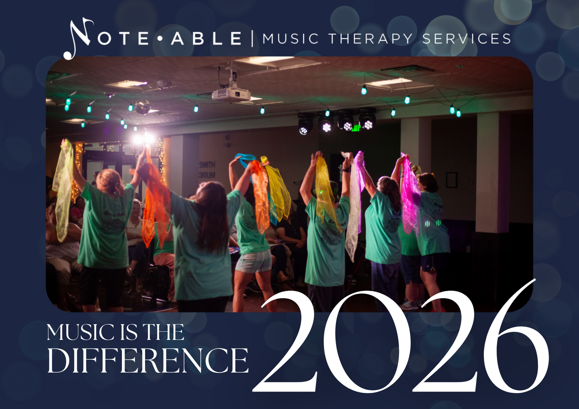 Group of children performing a dance with colorful scarves on stage, with a sign behind them reading ‘SMITH ORIUM’ and string lights overhead, for a music therapy event in 2020.