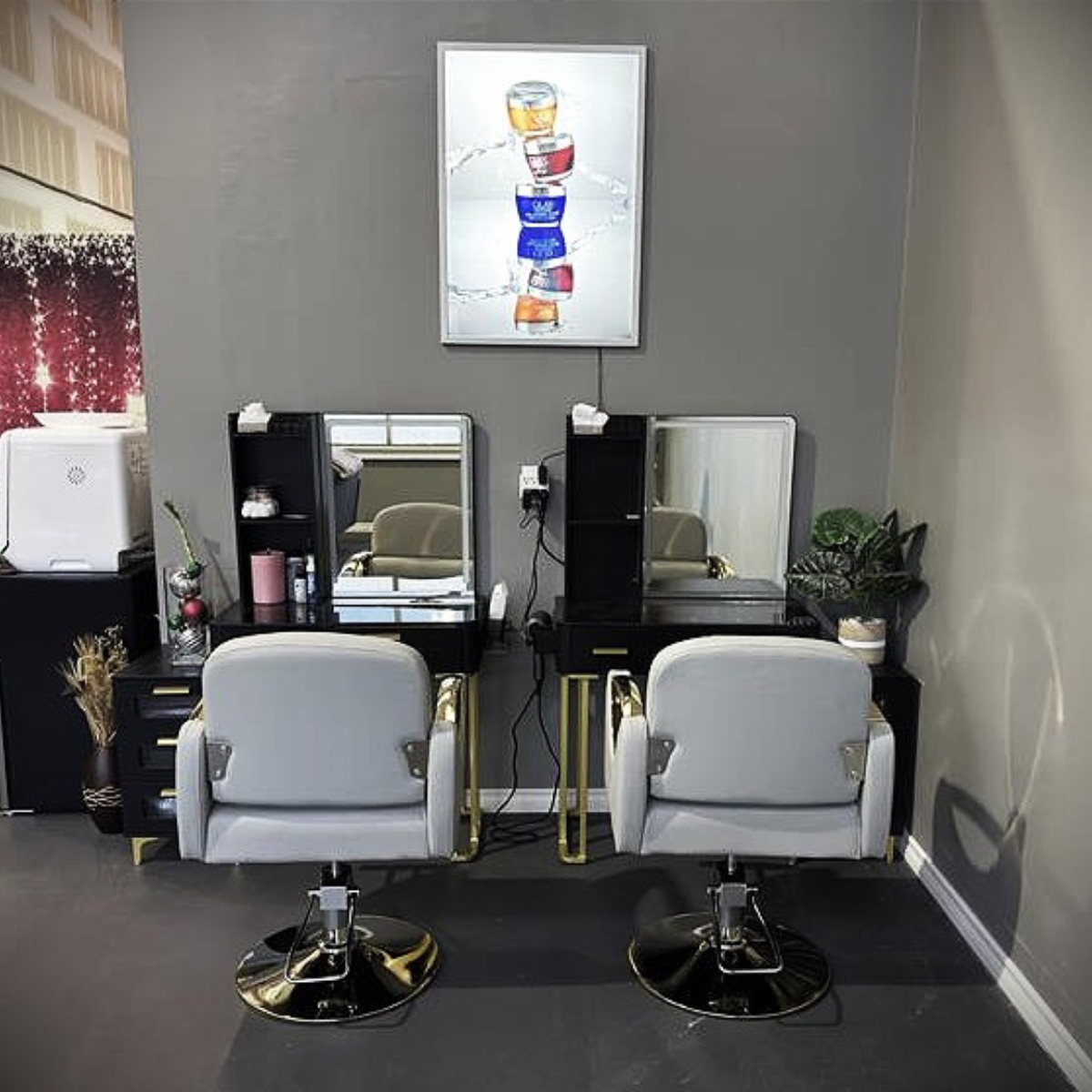 Two salon styling stations with white chairs, black and gold mirrors, and small black tables with shelves, set against a gray wall. Above, a framed art piece depicts colorful stacked stones.