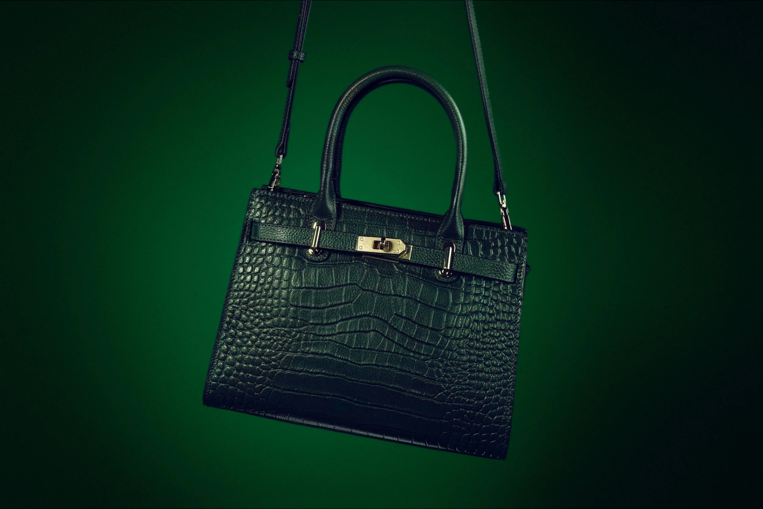 Black crocodile leather handbag with silver hardware hanging against a green background