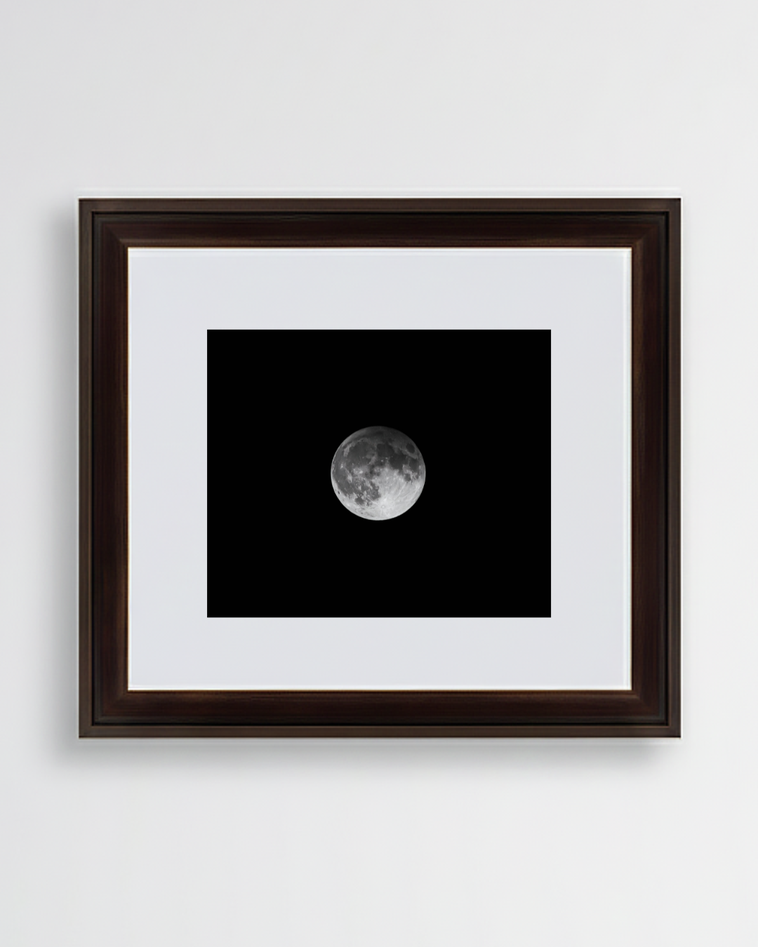 Photograph of a framed picture of the full moon on a black background hanging on a white wall.