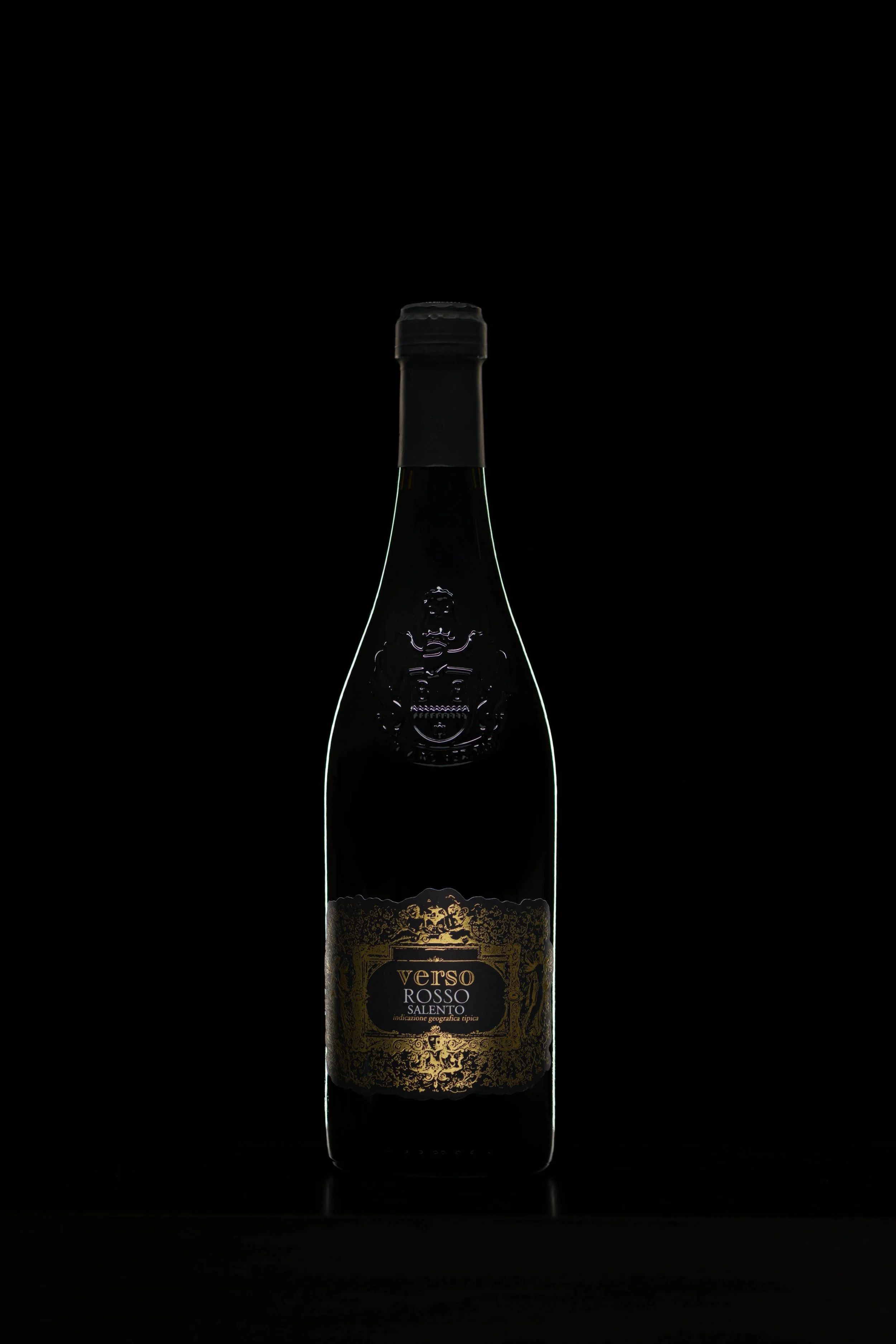 Dark glass wine bottle with a gold label, labeled 'Verso Rosso Salento,' on a black background, lit subtly highlighting the edges.