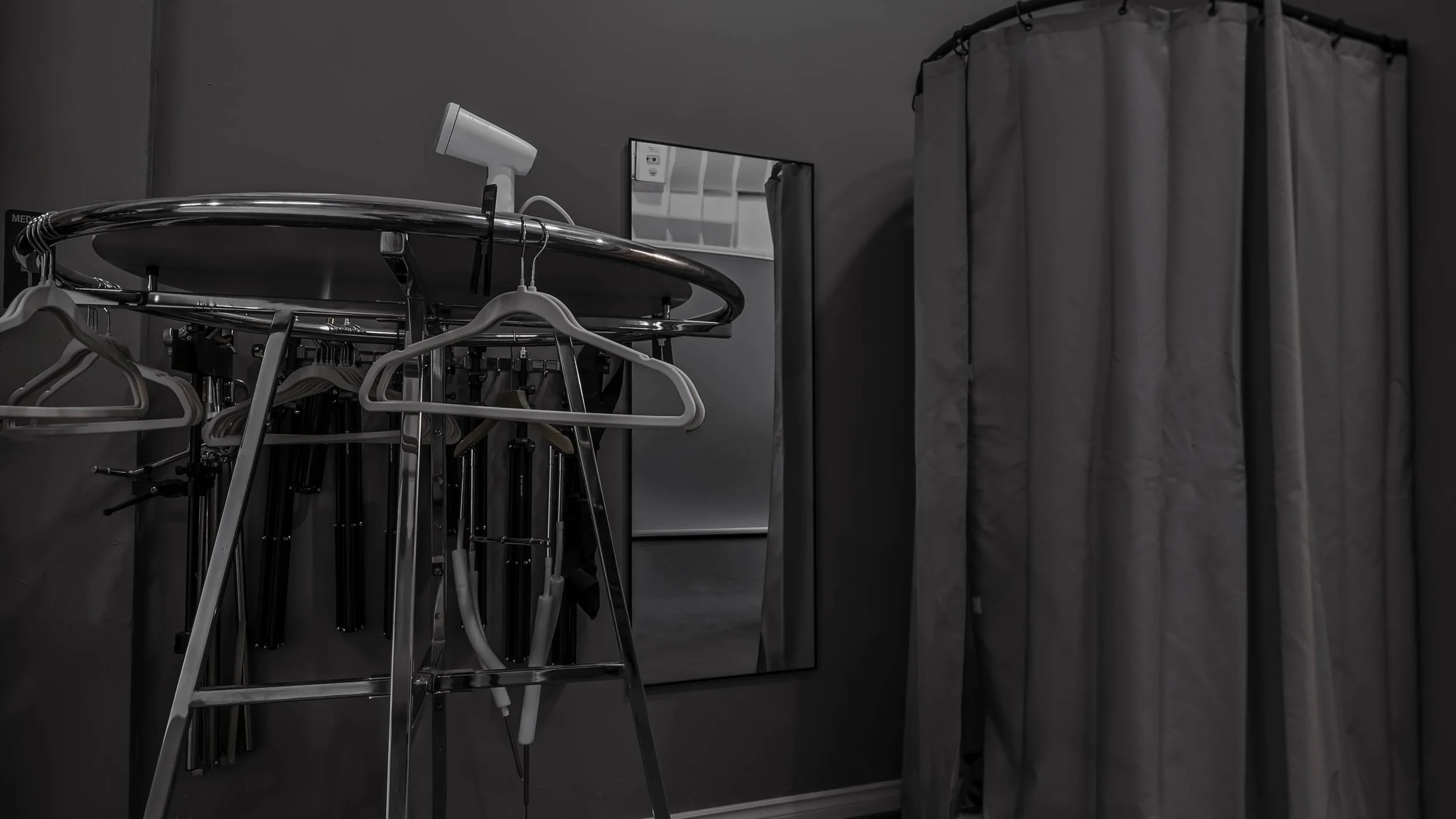 Medical examination room with a gray curtain, wall mirror, and a mobile stand holding medical or dental tools, including a thermometer and gloves.