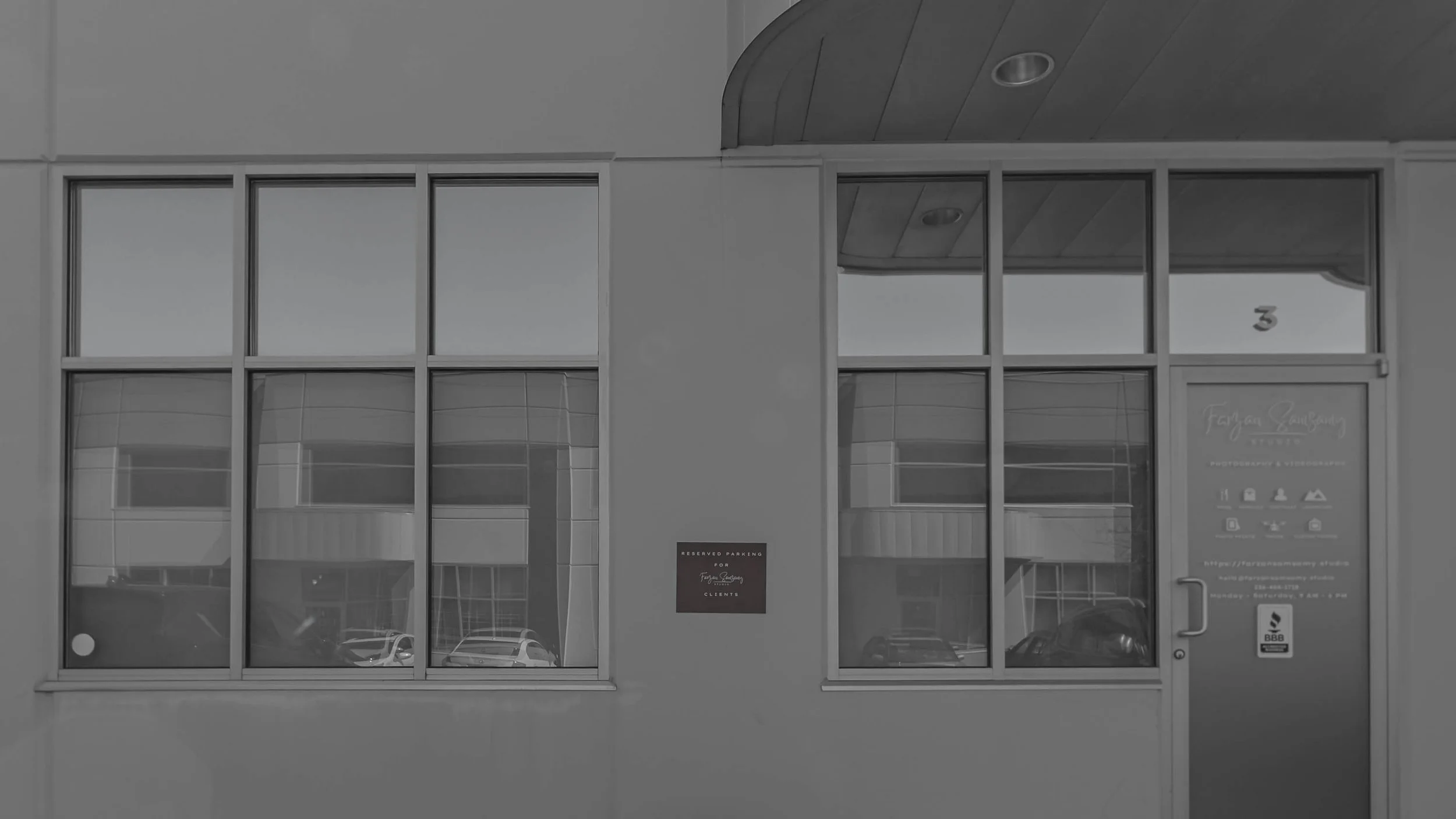 Front view of a building with large glass windows and a door, including signs indicating reserved parking for clients and business information.