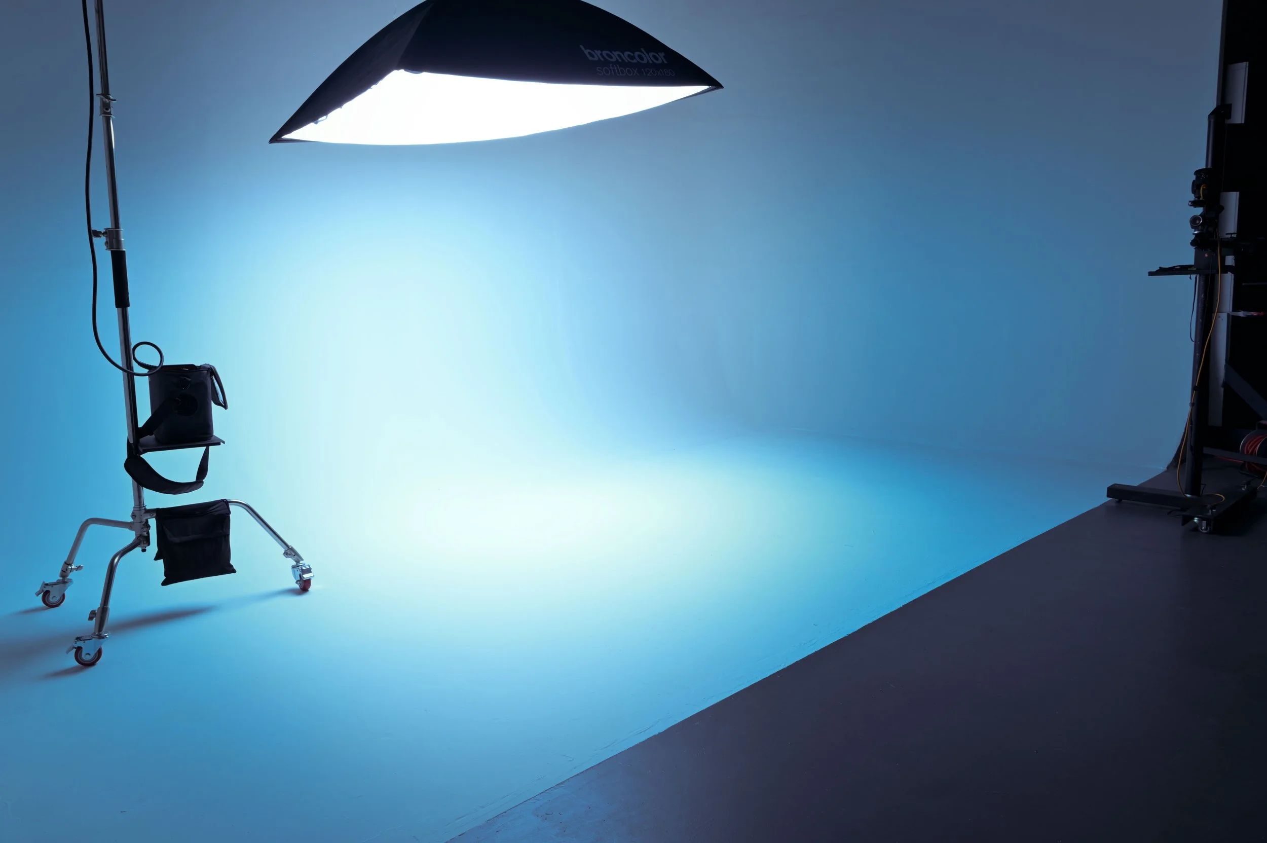 Photography studio with a blue backdrop, professional lighting equipment, a mobile lighting stand, and camera gear.