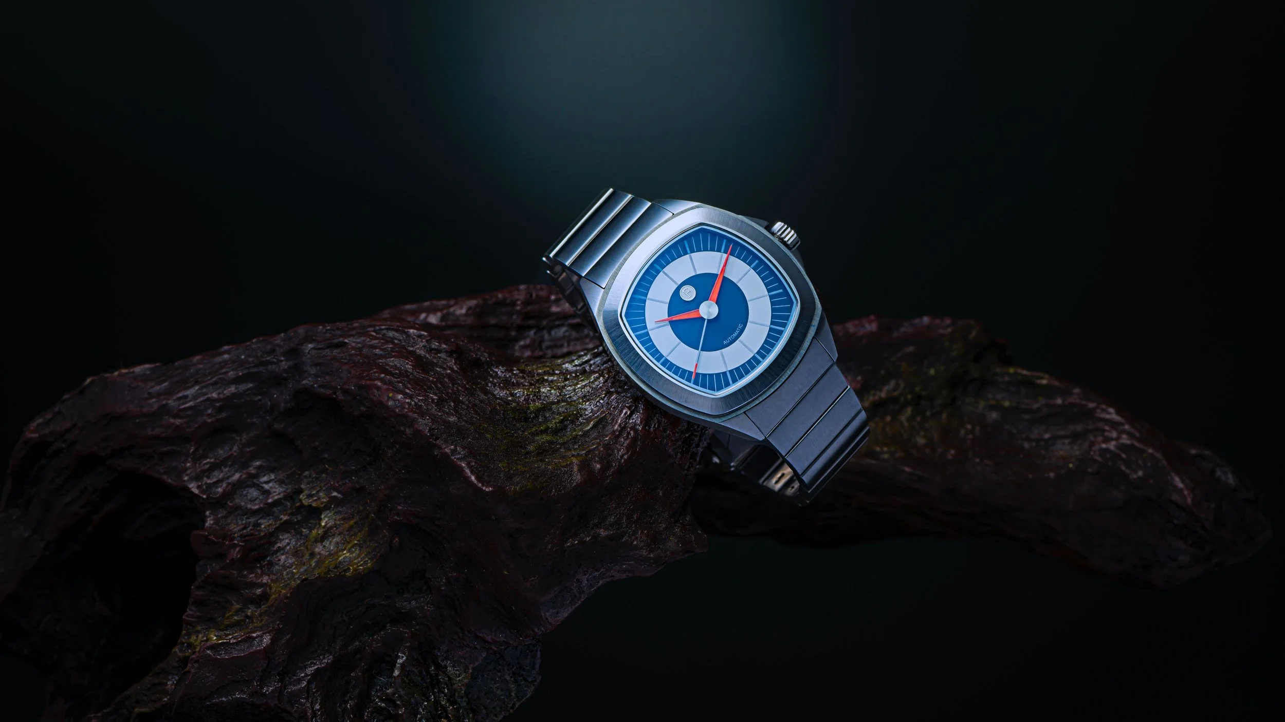 A blue and silver wristwatch resting on a dark, textured piece of wood against a black background.