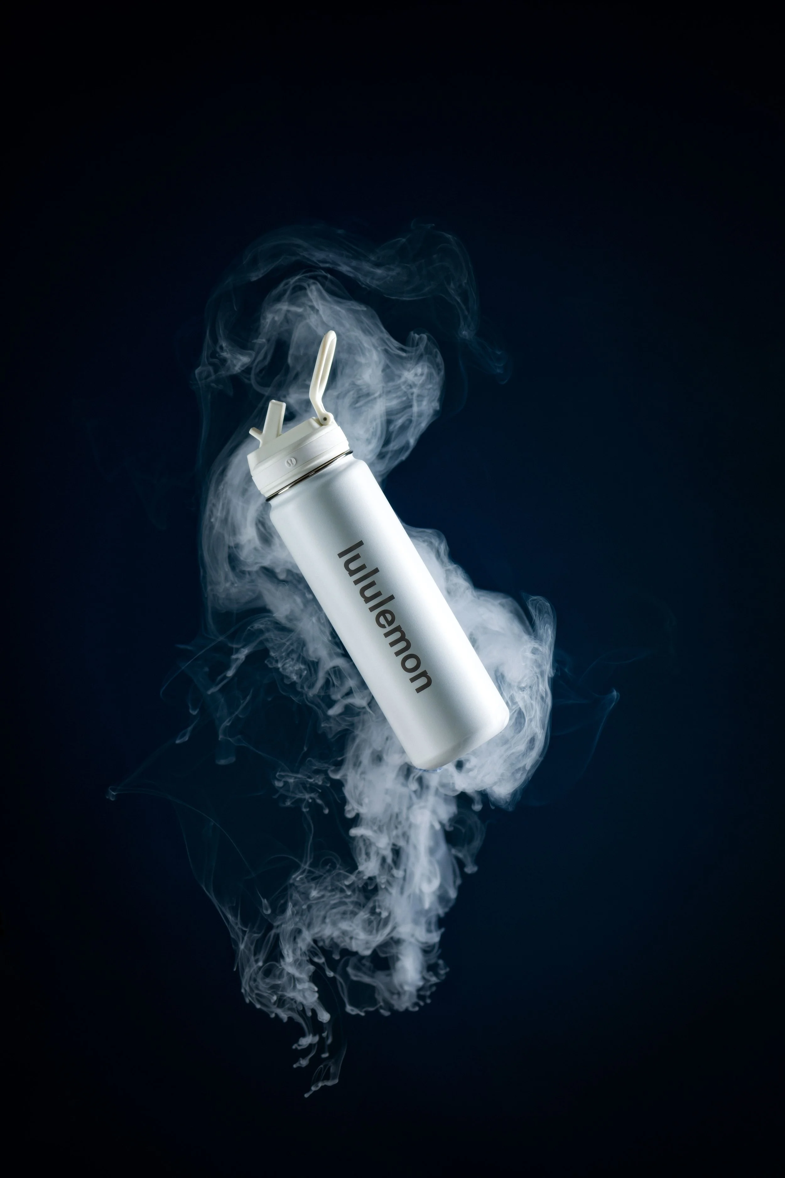 A white zippo-style lighter labeled 'lulem', releasing vapor or smoke, against a dark background.