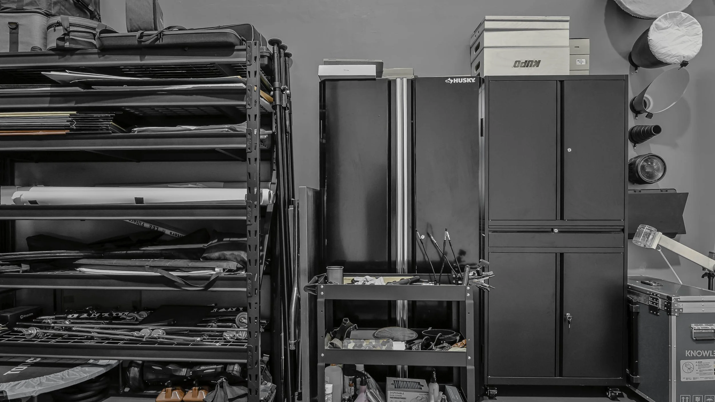 Black metal shelving unit filled with various tools, black cabinets, and storage boxes in a garage or workshop setting.