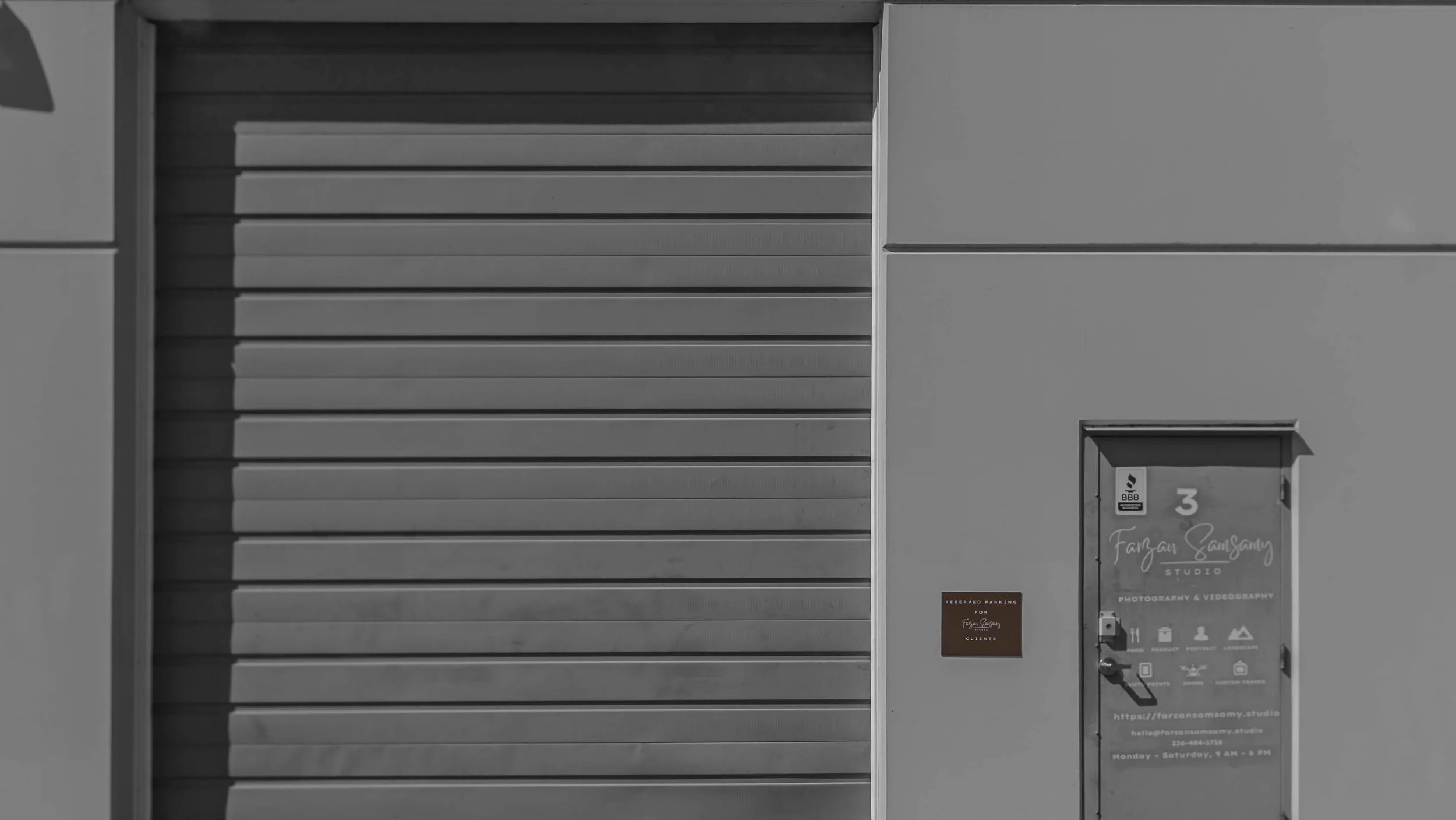 A metal garage door and a small door with signage for a photography studio, with a reserved parking sign nearby