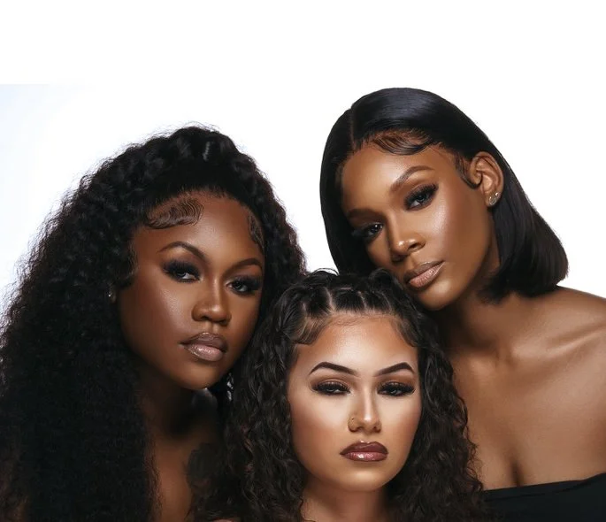 Three women with glamorous makeup and hairstyles posing closely together against a white background.