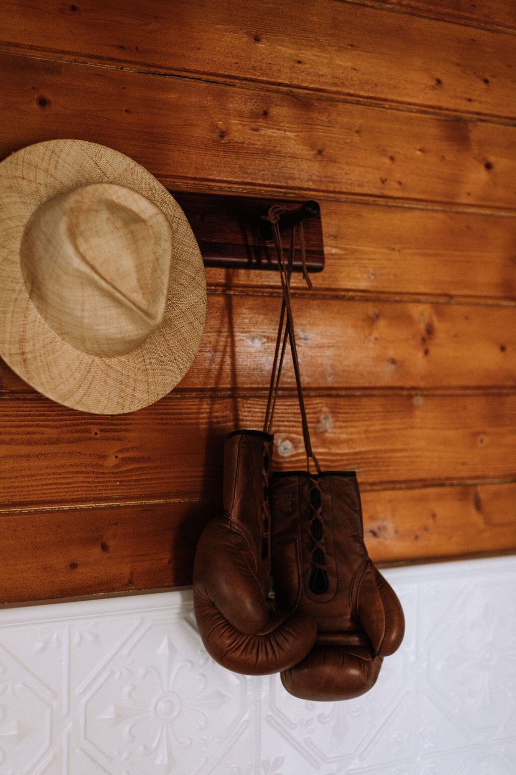 The Inn Beechworth, Luxury Accommodation - Kelly House Hallway with wooden wall with a straw hat and vintage brown boxing gloves hanging on hooks; white decorative panelling below.