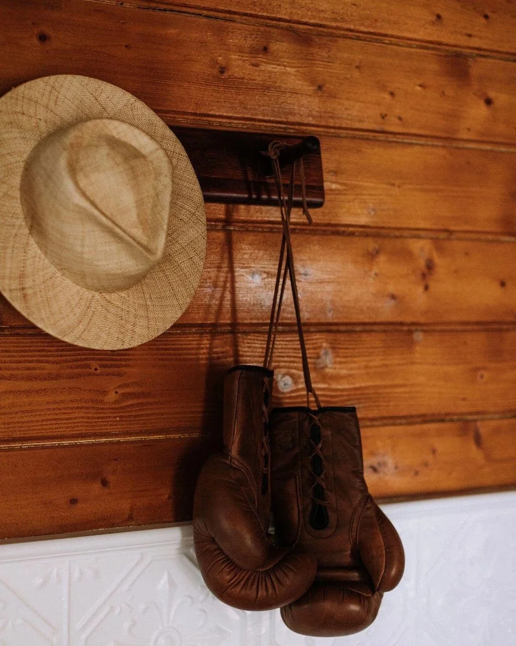 The Inn Beechworth, Luxury Accommodation - Kelly House Hallway with wooden wall with a straw hat and vintage brown boxing gloves hanging on hooks; white decorative panelling below.